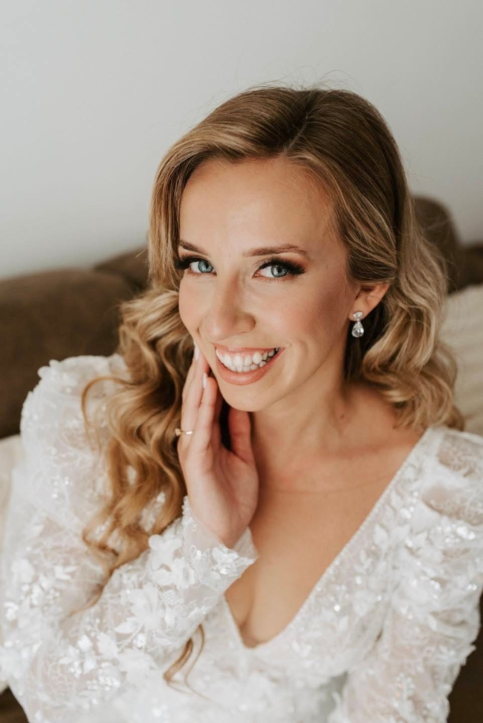 A bride in an elegant lace wedding dress with styled blonde curls and natural makeup.