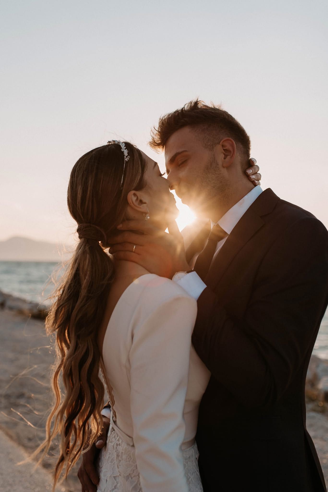 A romantic sunset kiss captured on a beach with mountains in the background.