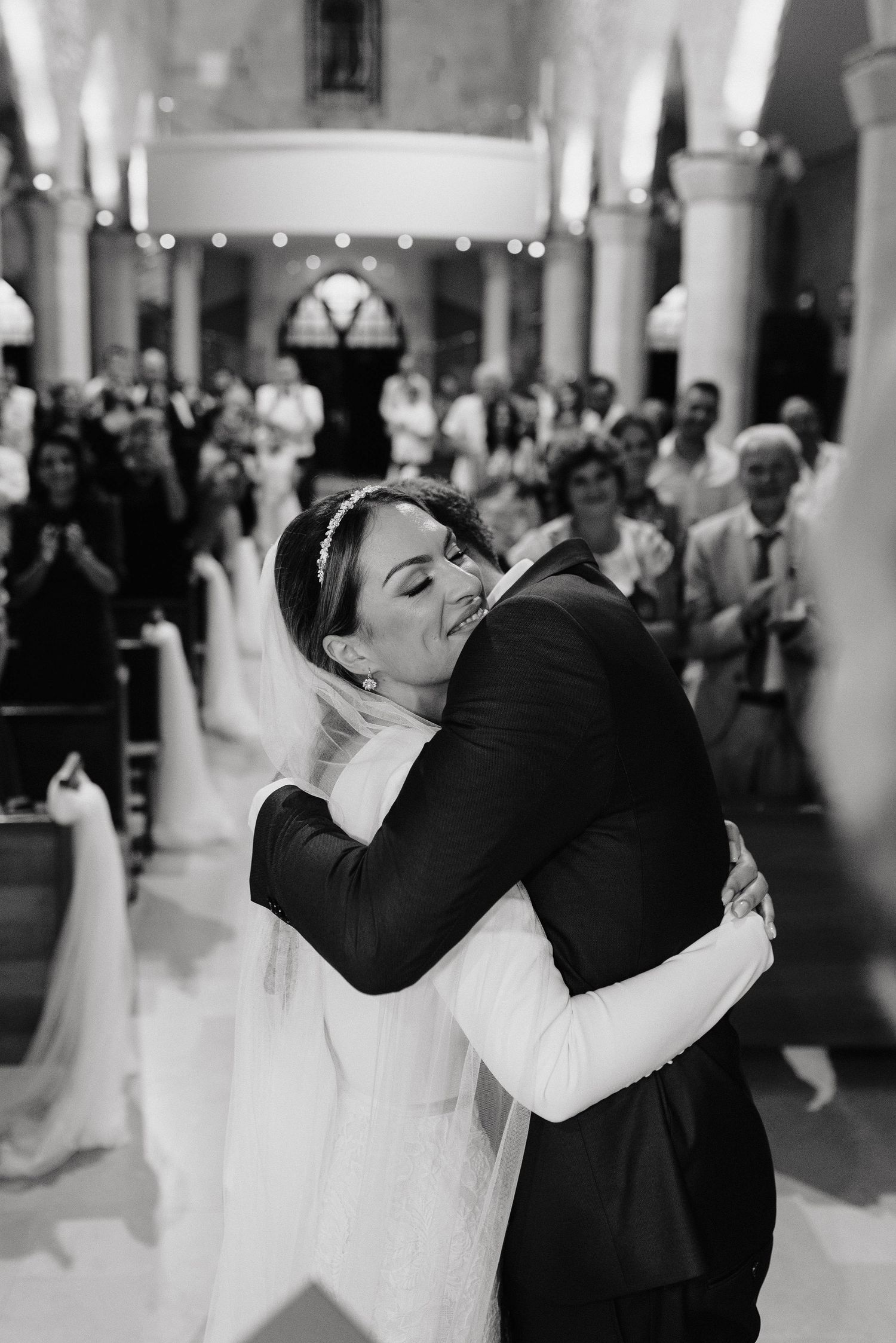 An emotional embrace during a wedding ceremony inside a traditional church with guests looking on.