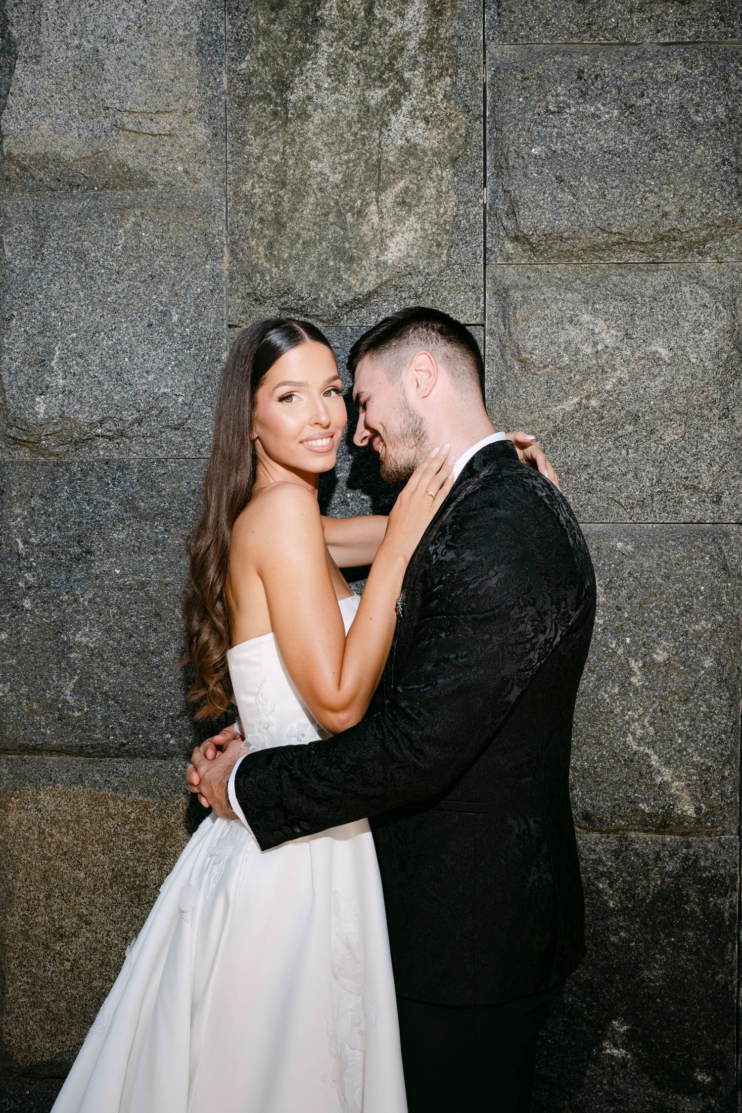 A couple in wedding attire share an intimate moment against a stone wall in a series of romantic photos.