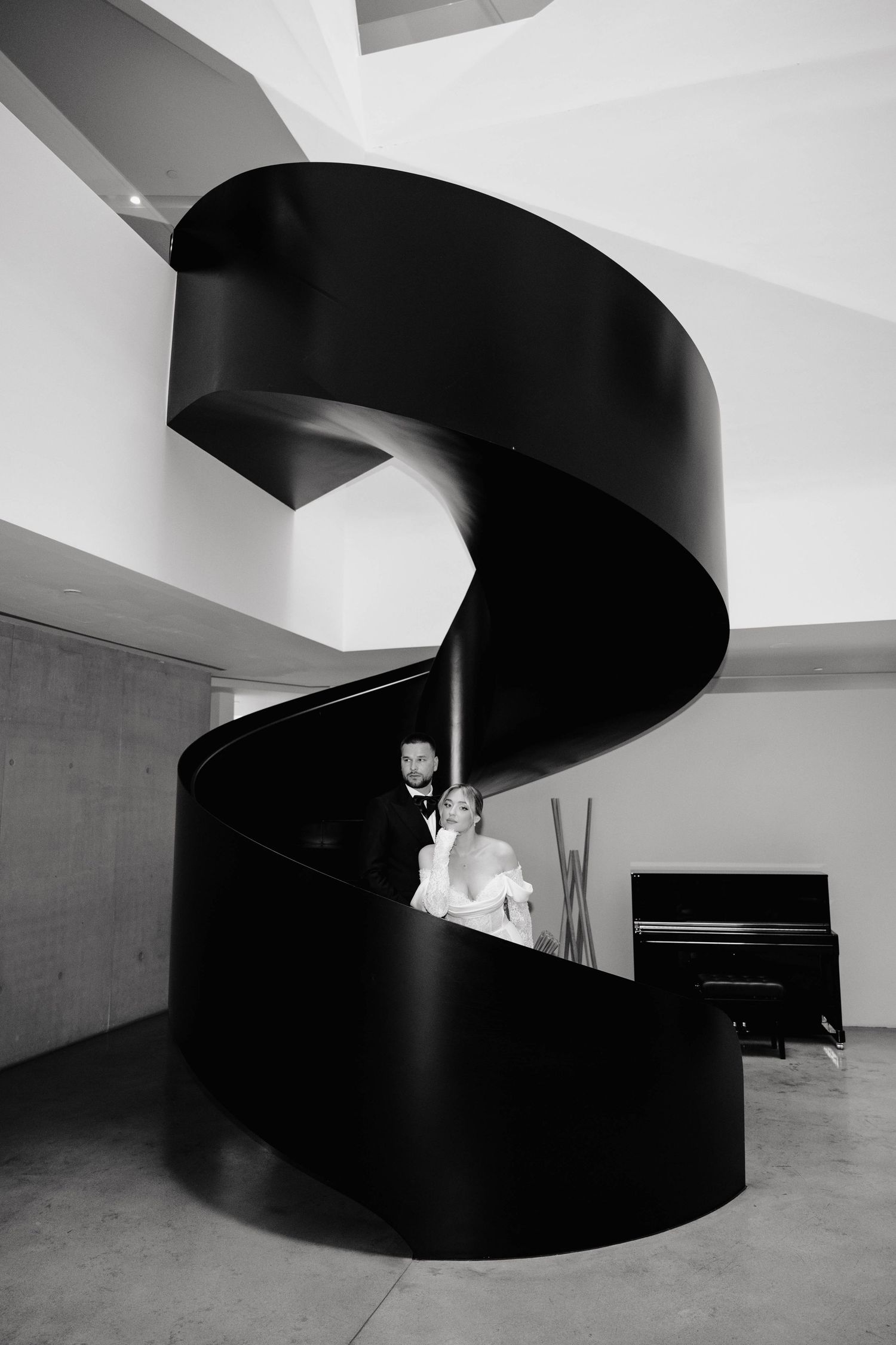 Black and white photo of a bride and groom posing on a dramatic spiral staircase at their wedding venue.