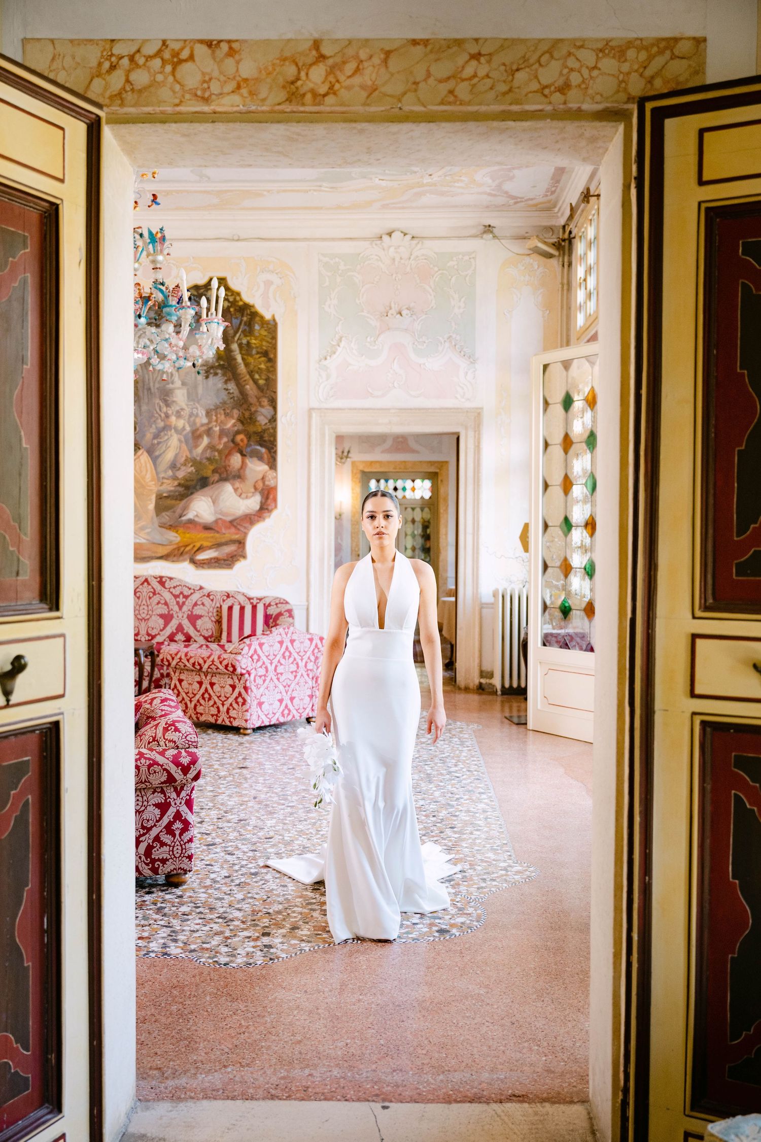 Elegant white halter wedding gown photographed in an ornate Italian villa with vintage decor and patterned tile floors.