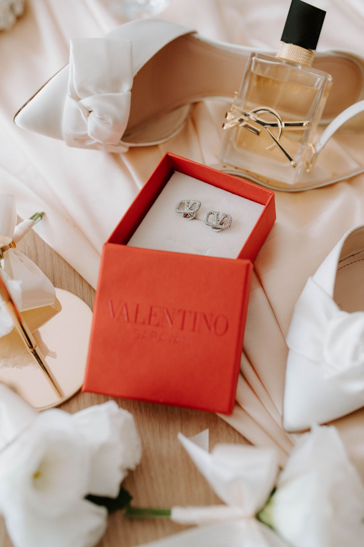 Valentino jewelry box with wedding rings displayed among white flowers and perfume bottle.