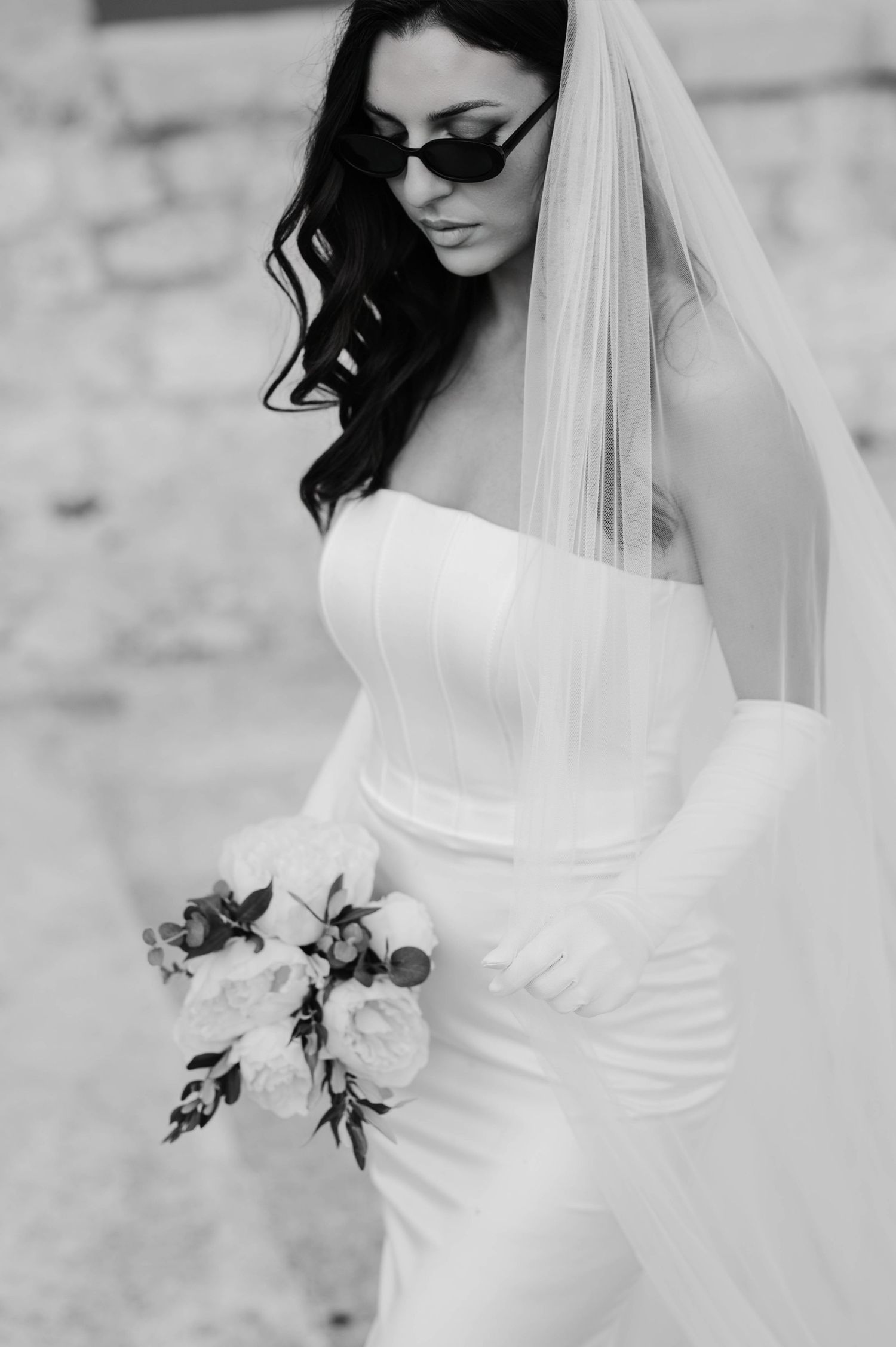A black and white bridal portrait with sunglasses and a classic fitted wedding gown.