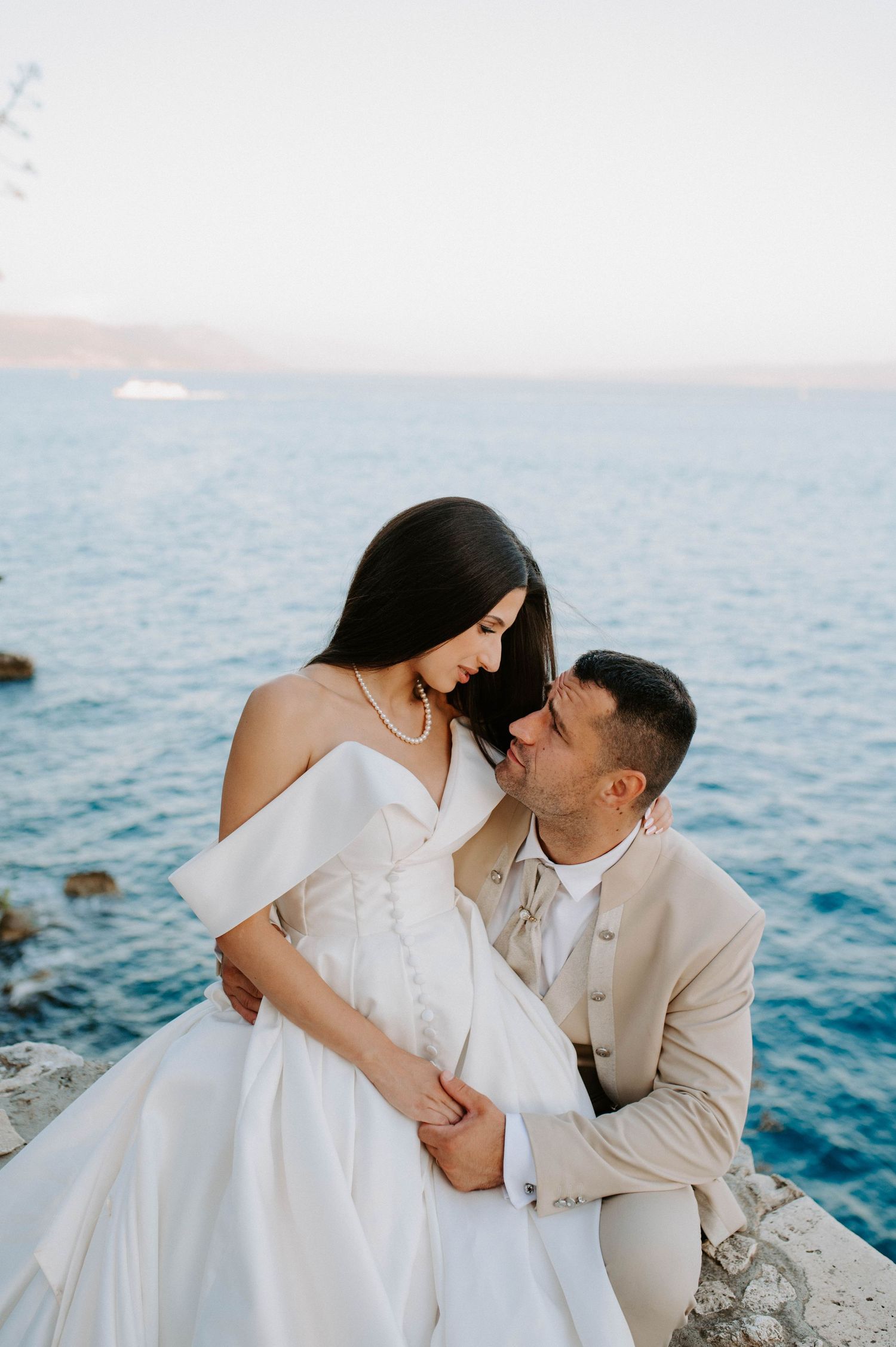 A couple in wedding attire shares an intimate moment by the Mediterranean Sea.