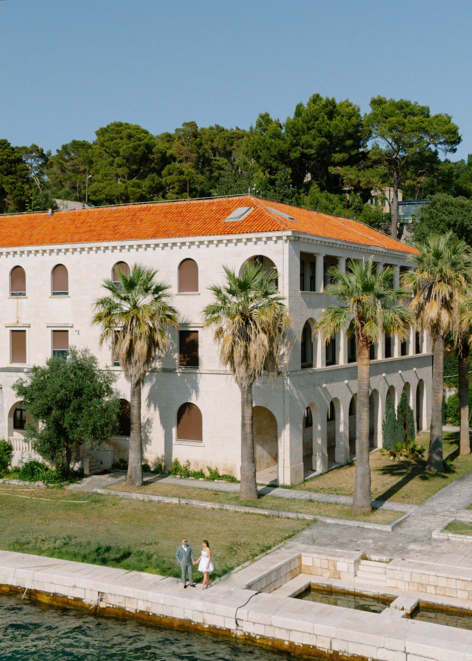 Historic Mediterranean-style building with white arches and palm trees along a waterfront promenade in Florida.