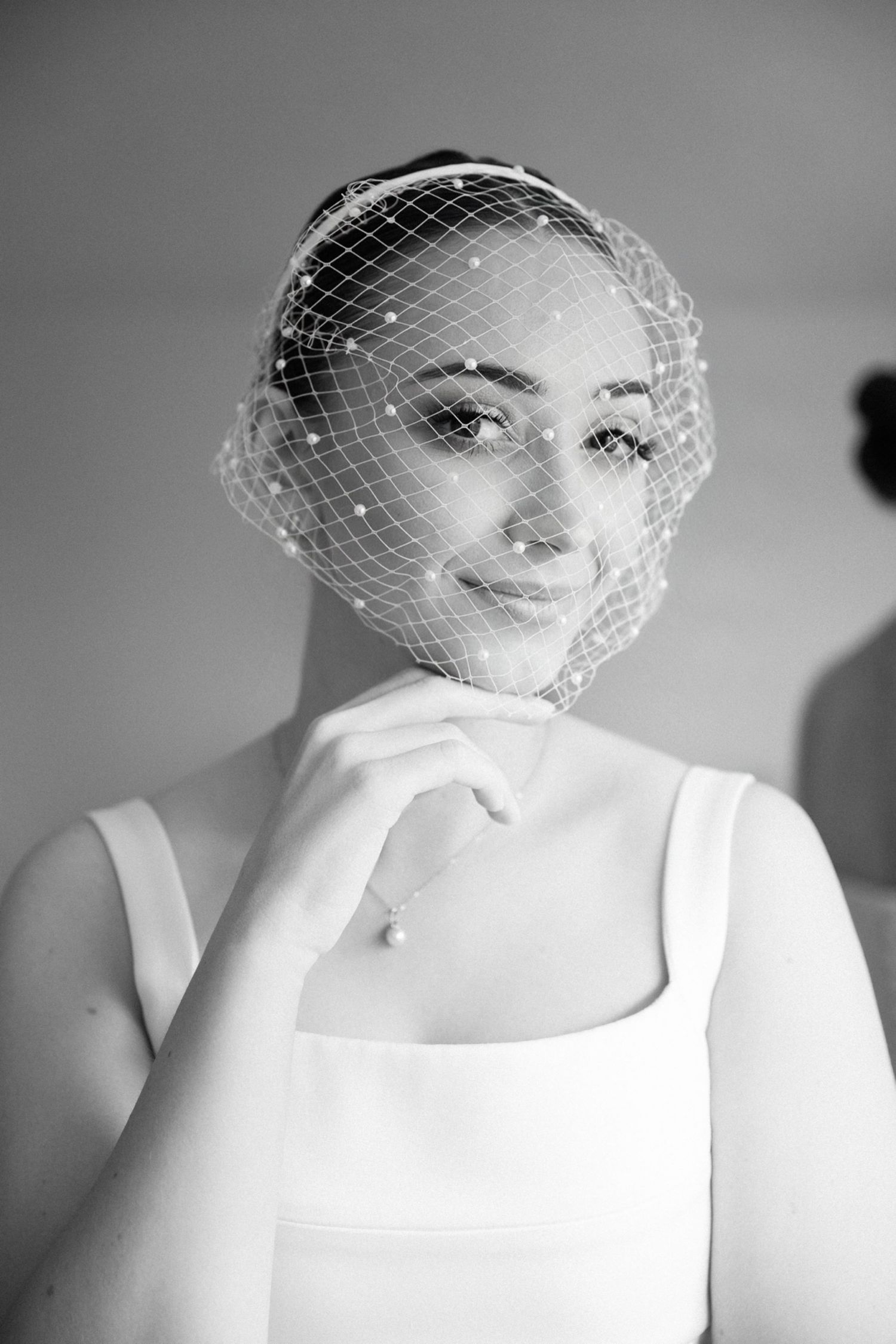 Black and white portrait of a person wearing a delicate white birdcage veil.