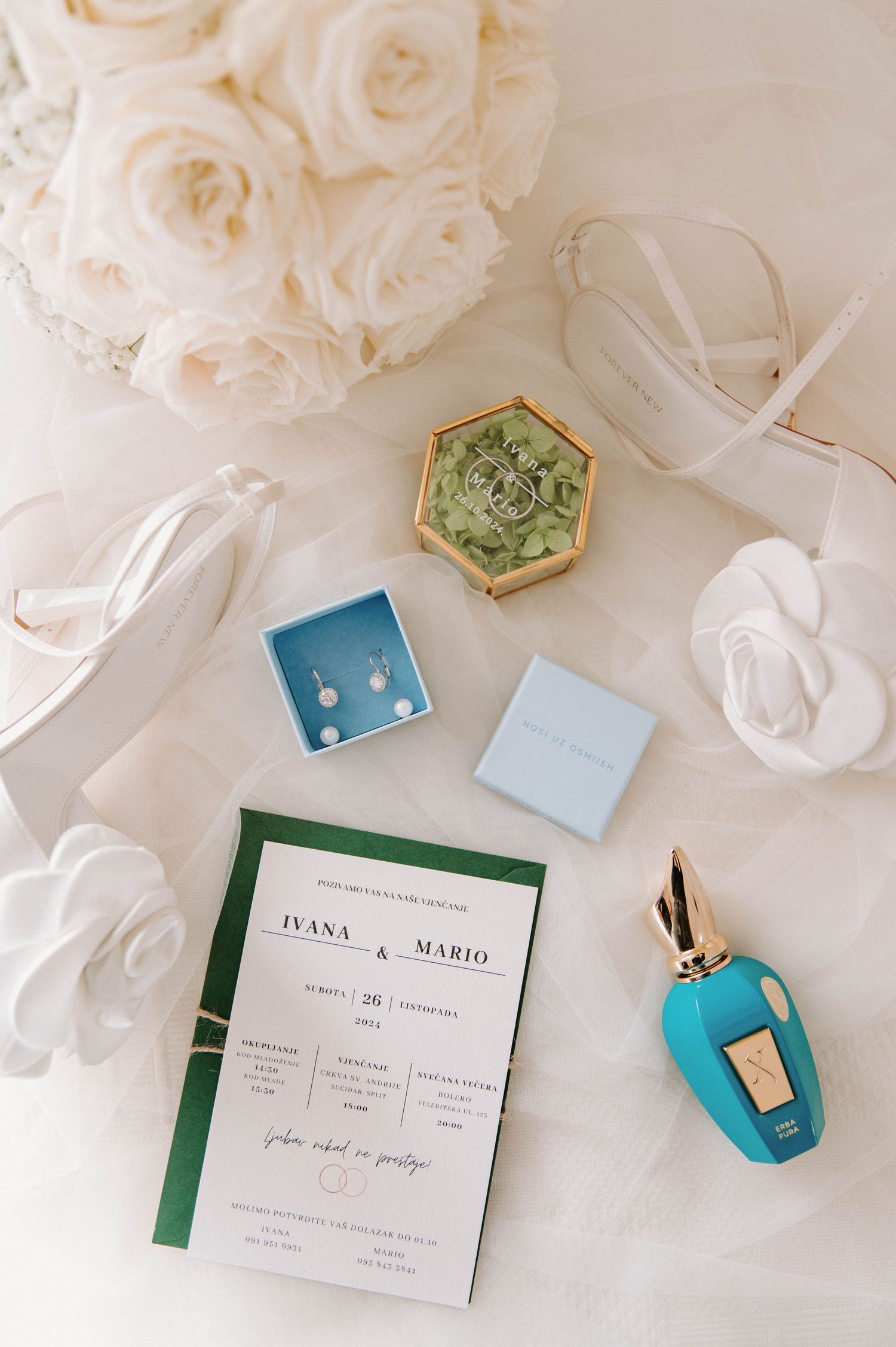 Wedding details flatlay with white roses, invitation, jewelry boxes and turquoise car key on light background.