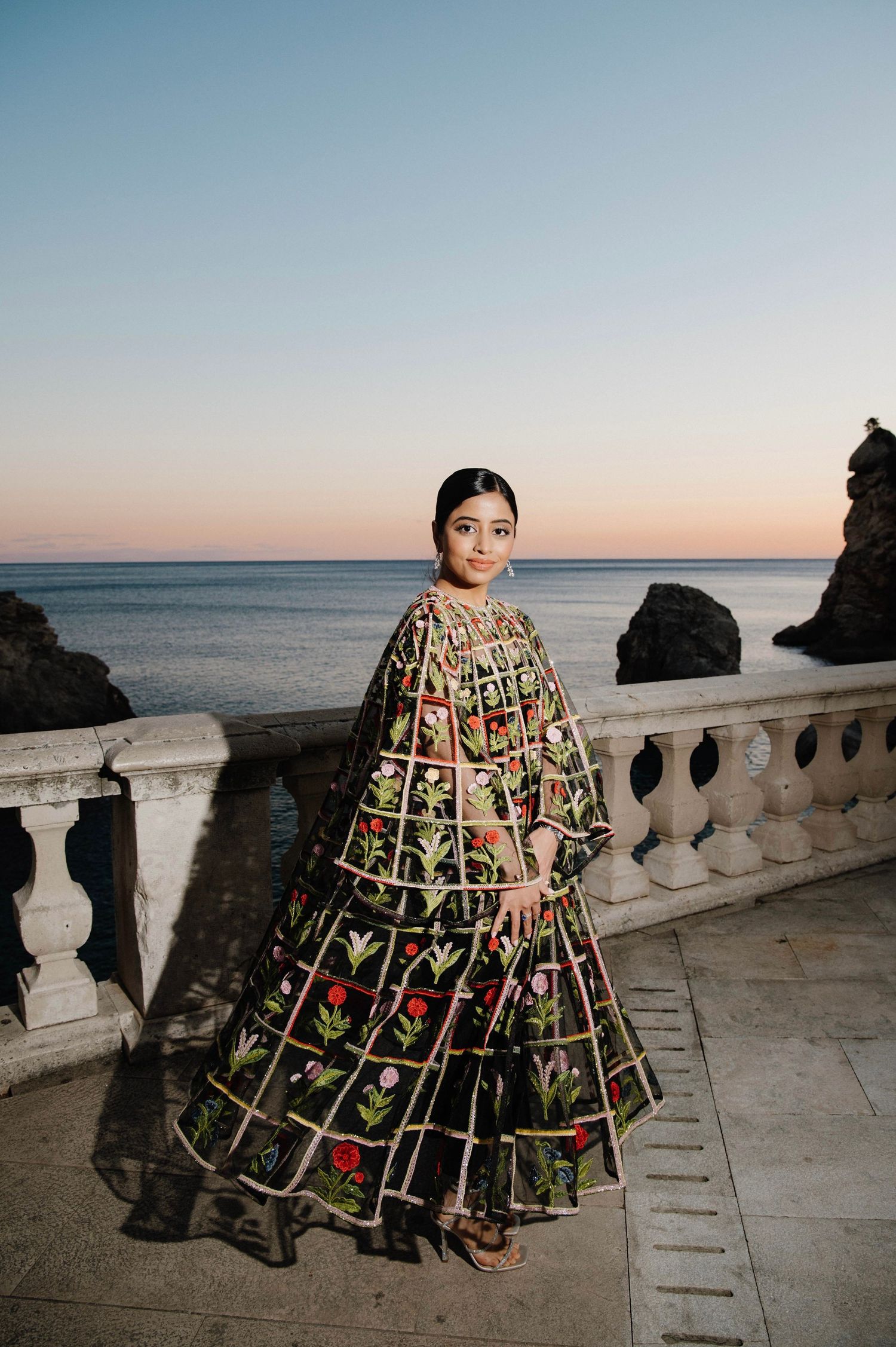 A floral patterned full-length gown photographed against an ocean backdrop at sunset.