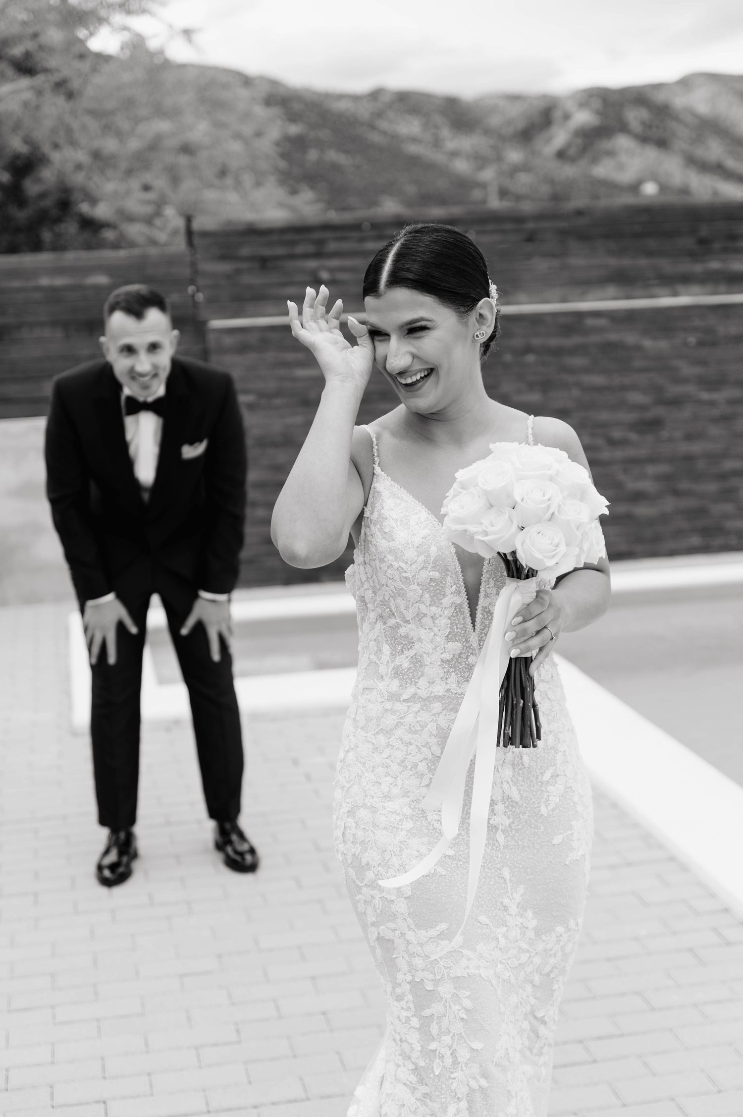 Candid black and white wedding moment captured on outdoor terrace with mountain backdrop.