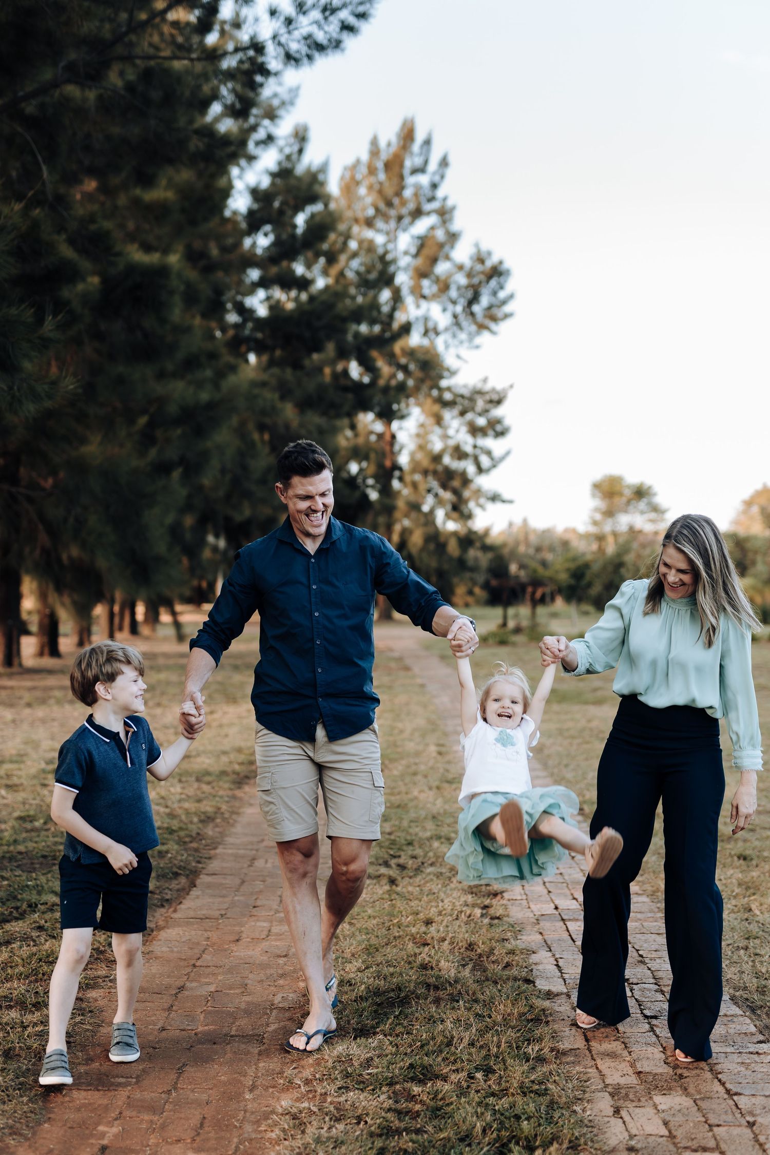 A playful candid portrait series shows adults and children walking and interacting along a tree-lined outdoor path.