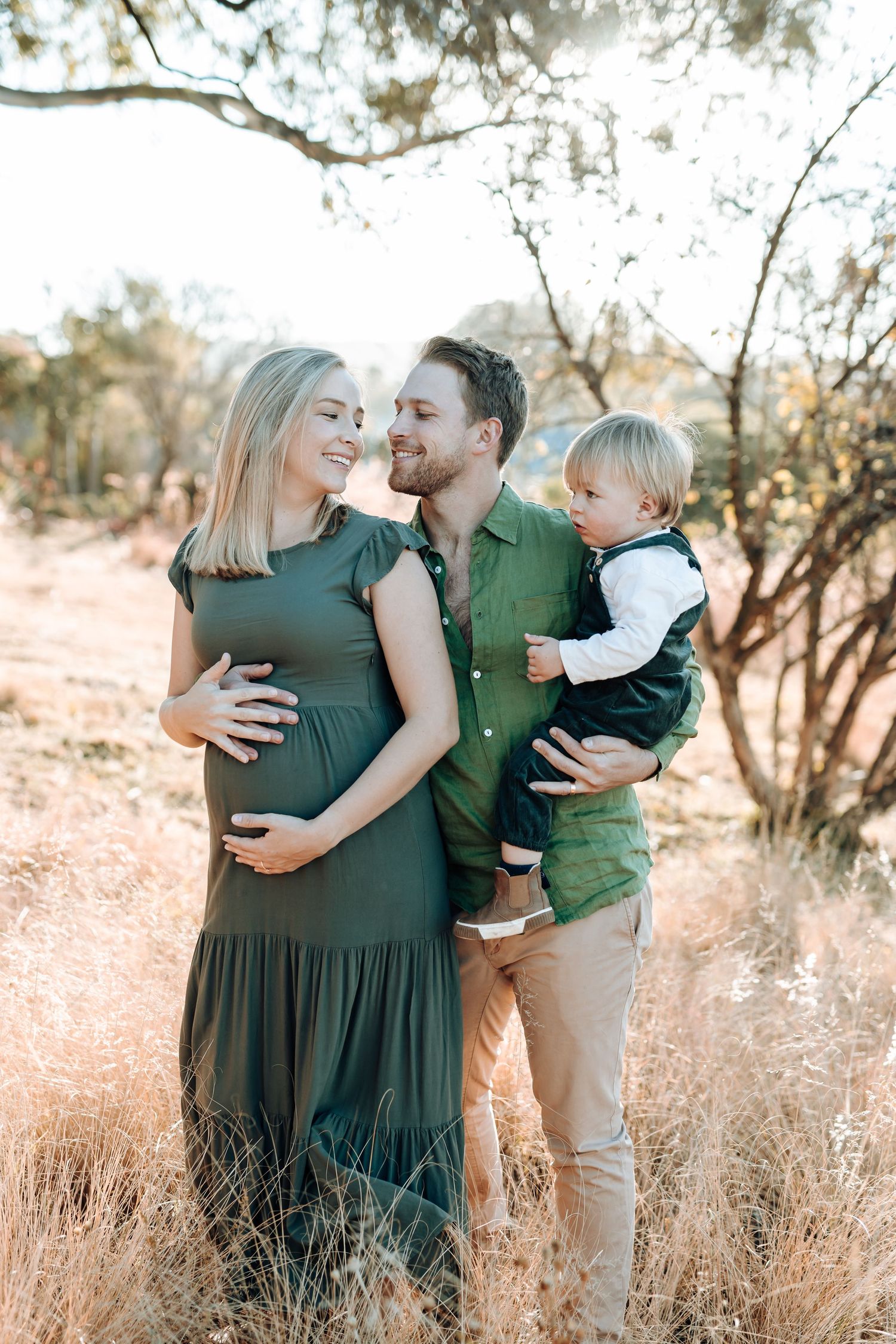 Loving family embraces in golden sunlit field with tall grass and desert trees creating a warm autumn atmosphere.