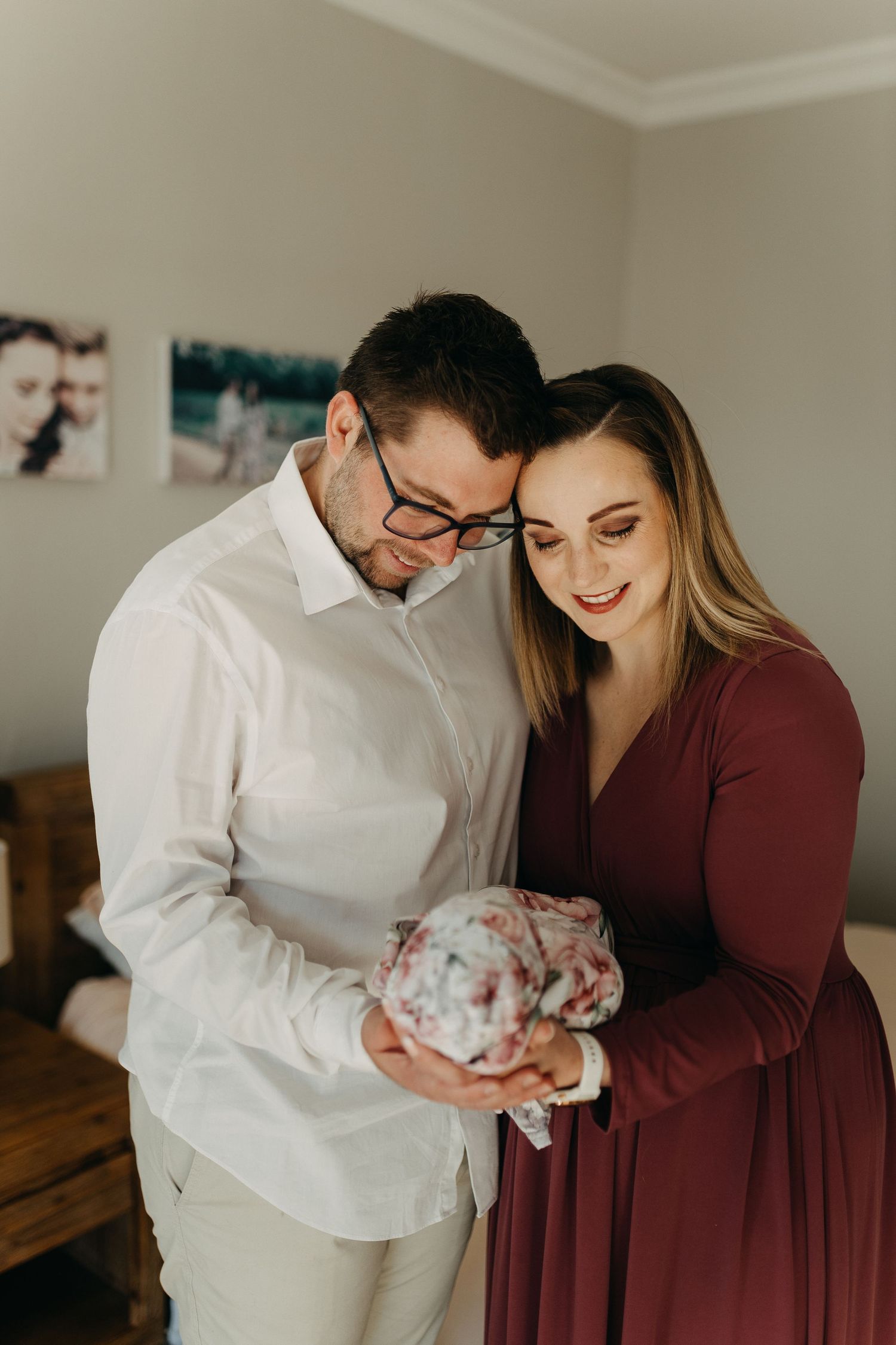 A couple in maroon and white clothing tenderly holding their newborn baby indoors.