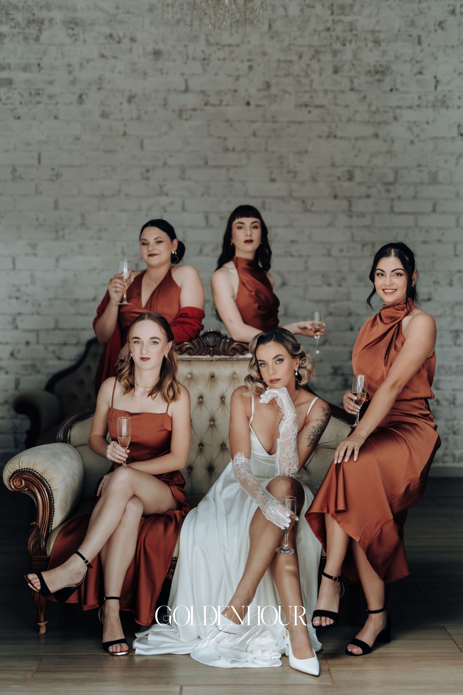 Bridal party lounges on vintage furniture wearing burgundy dresses alongside the bride in white.