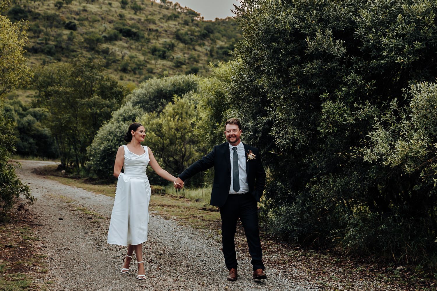 A couple walking together on a scenic outdoor path surrounded by lush green foliage.