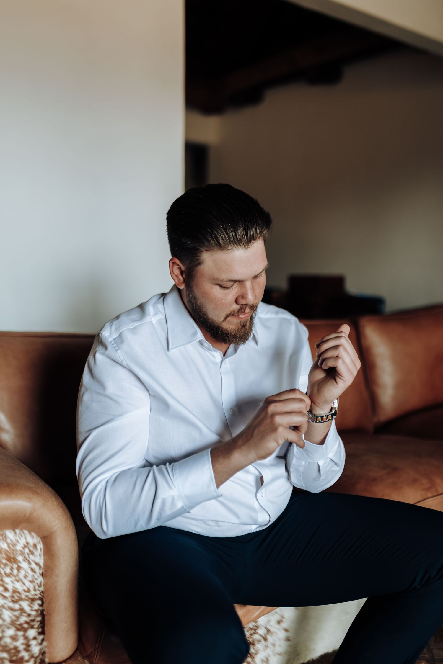 A person wearing a white shirt is seen sitting in a dark room contemplating with their head leaned down.