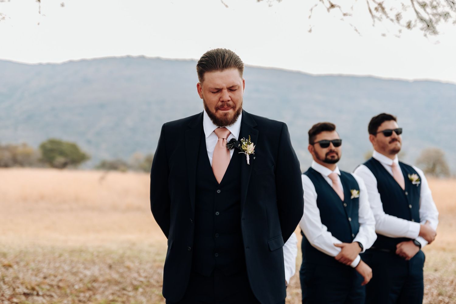 A group in formal attire walks together outside with mountains and a road visible in the background.