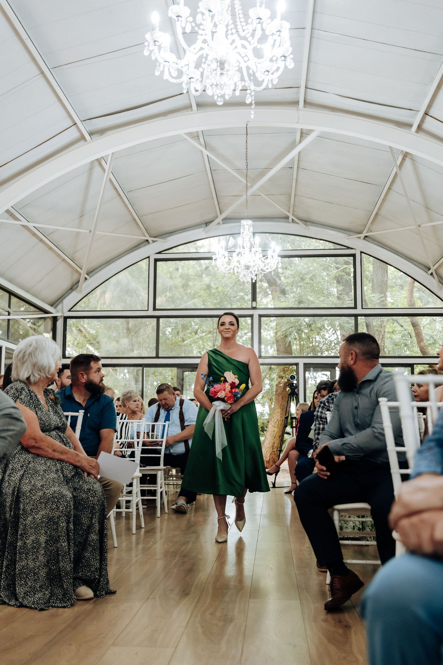 Wedding guests dance together in an elegant white-walled venue with crystal chandeliers overhead.