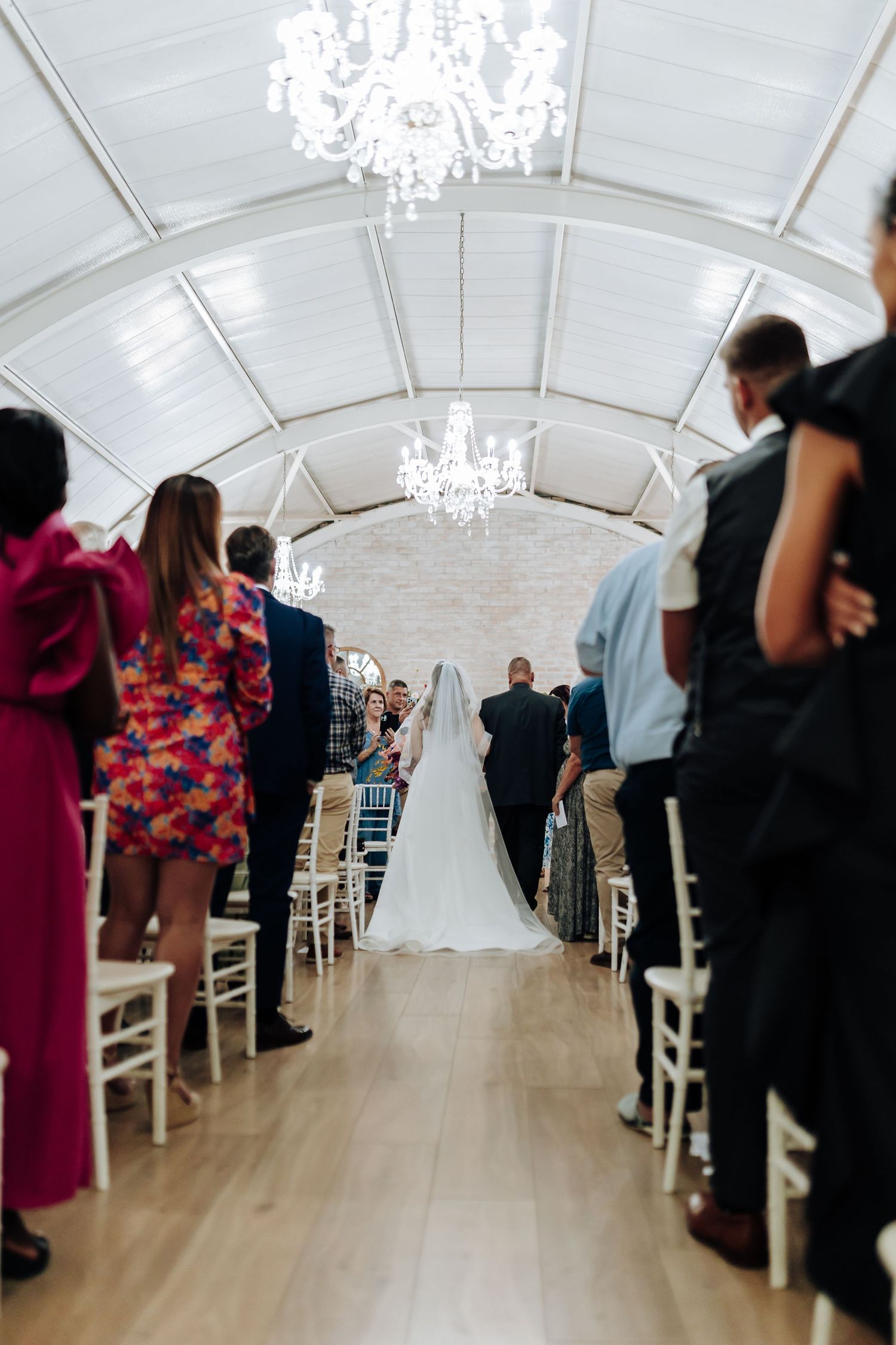 Wedding ceremony setup in a bright white venue with elegant chandeliers and floral decorations.
