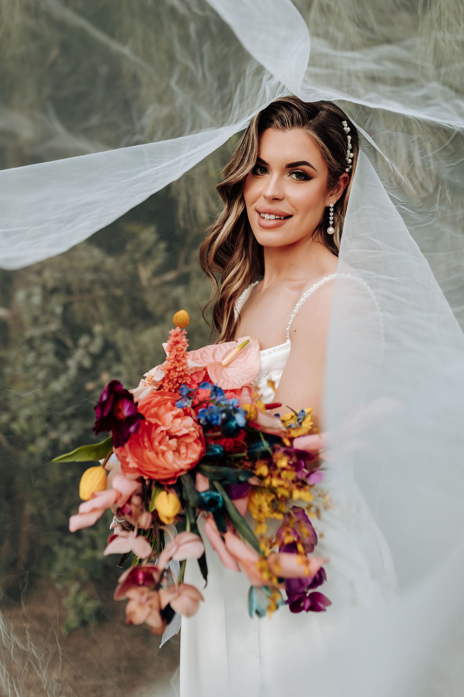 Ethereal bridal portraits showcase flowing veil and vibrant colorful bouquet with pink, orange, and blue flowers in mountain setting.