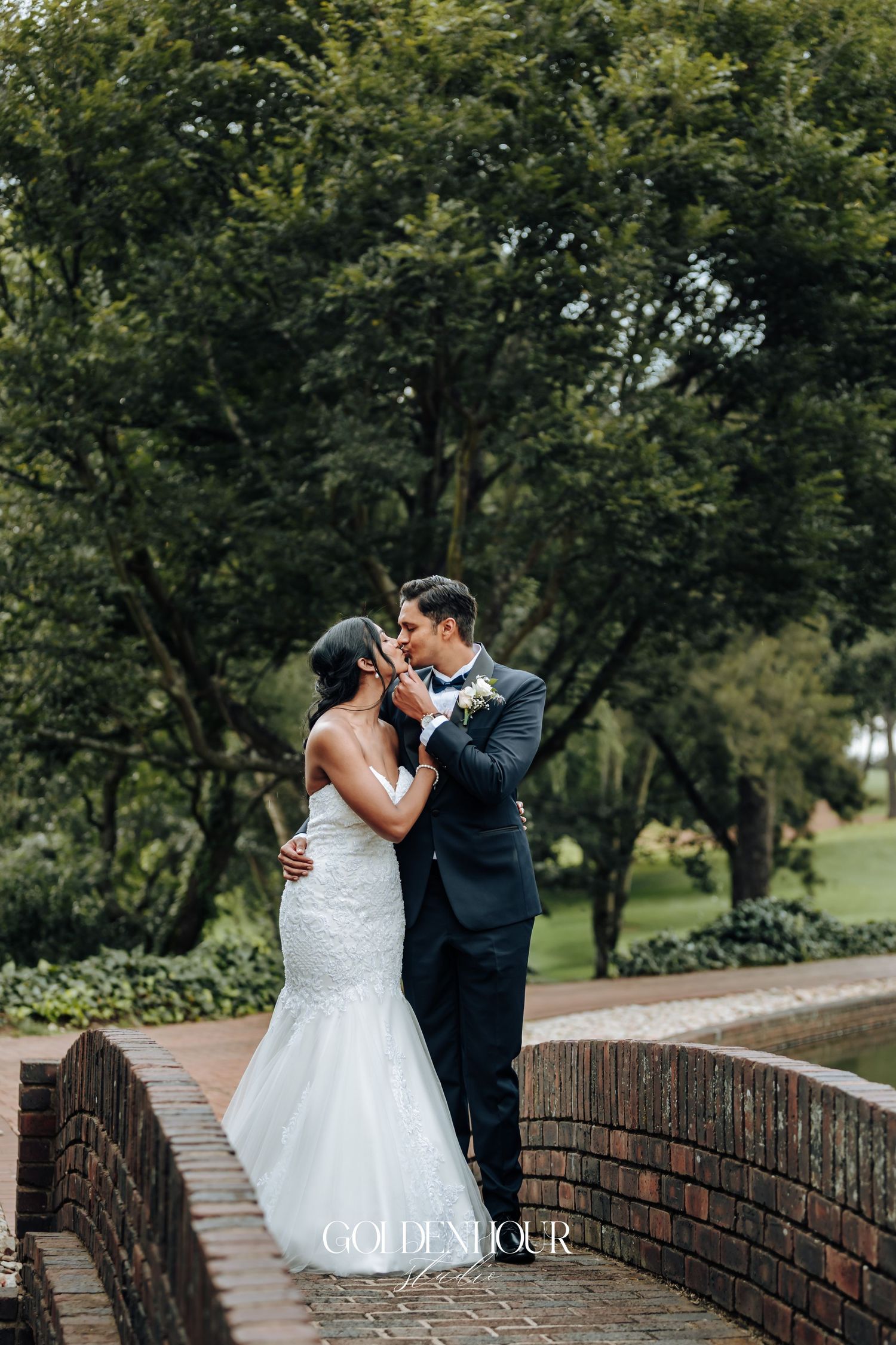 Romantic wedding couple sharing a moment on a brick bridge surrounded by trees.