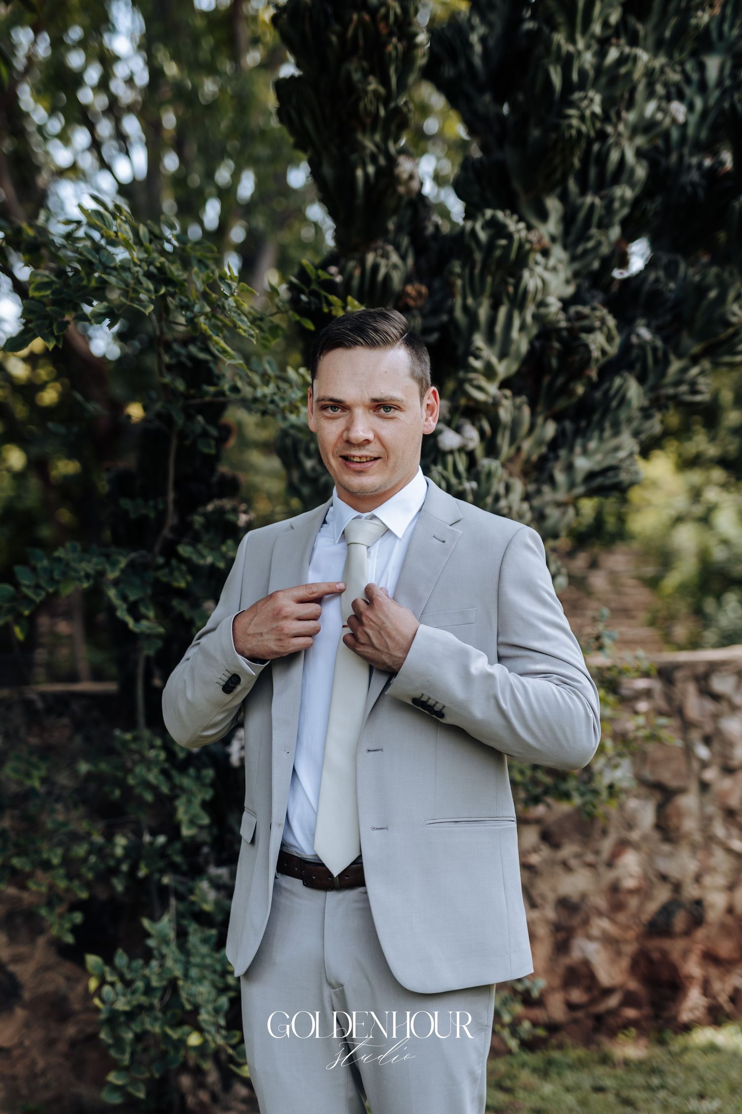 Wedding preparation scene showing a light gray suit jacket being adjusted outdoors.