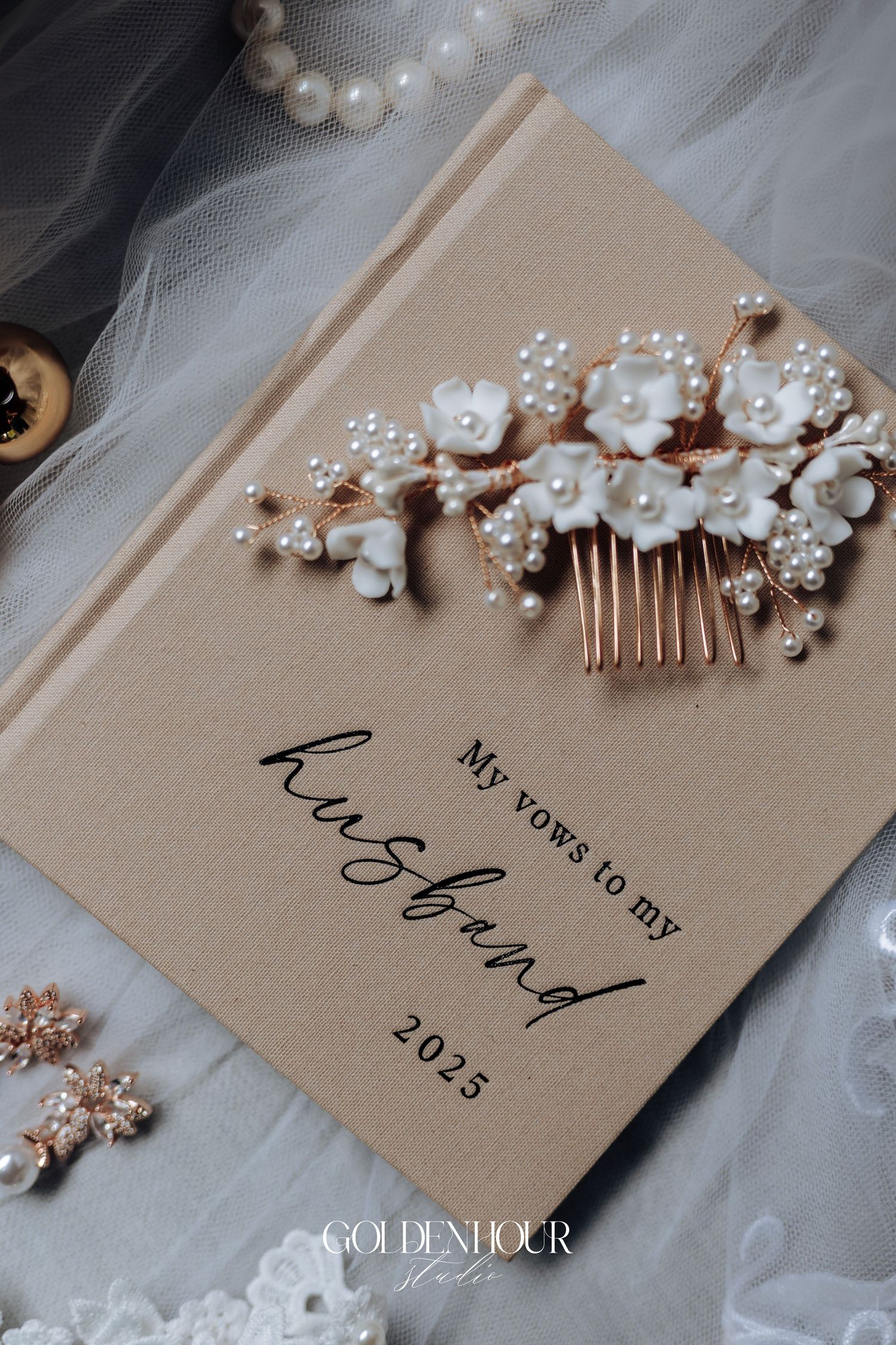 A delicate pearl hair comb rests on a beige wedding vows book with elegant calligraphy.