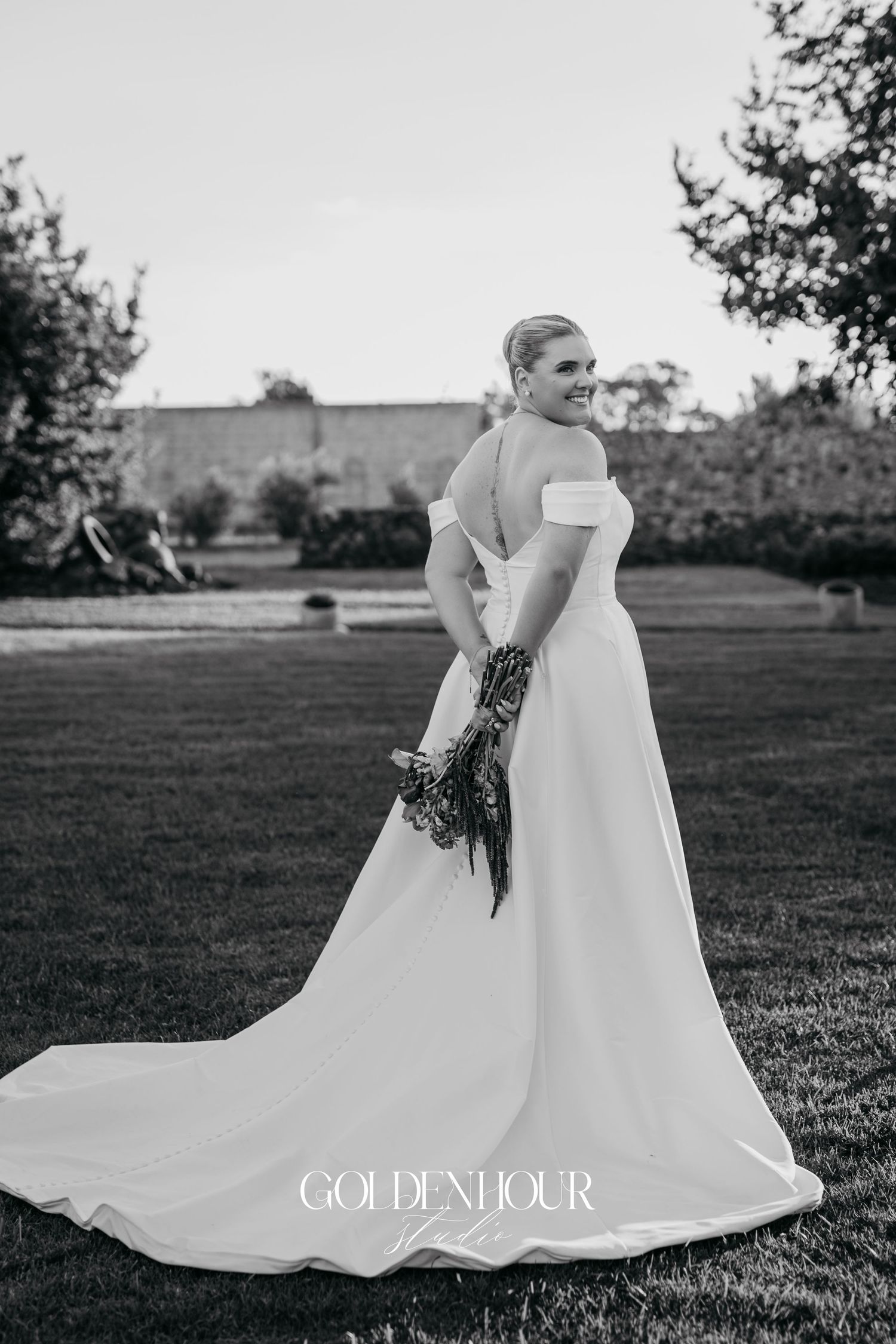 Black and white wedding photo series showing flowing white bridal gown with dramatic train in outdoor garden setting.