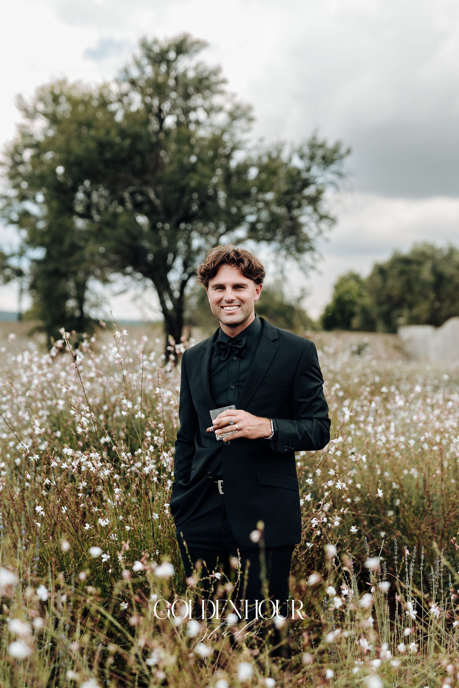 A person in black attire sits in a field of white wildflowers on an overcast day.