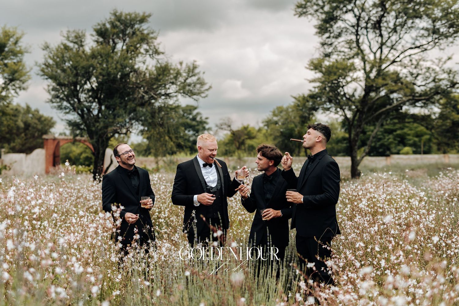 A group in black attire poses together in a blooming wildflower field on a cloudy day.