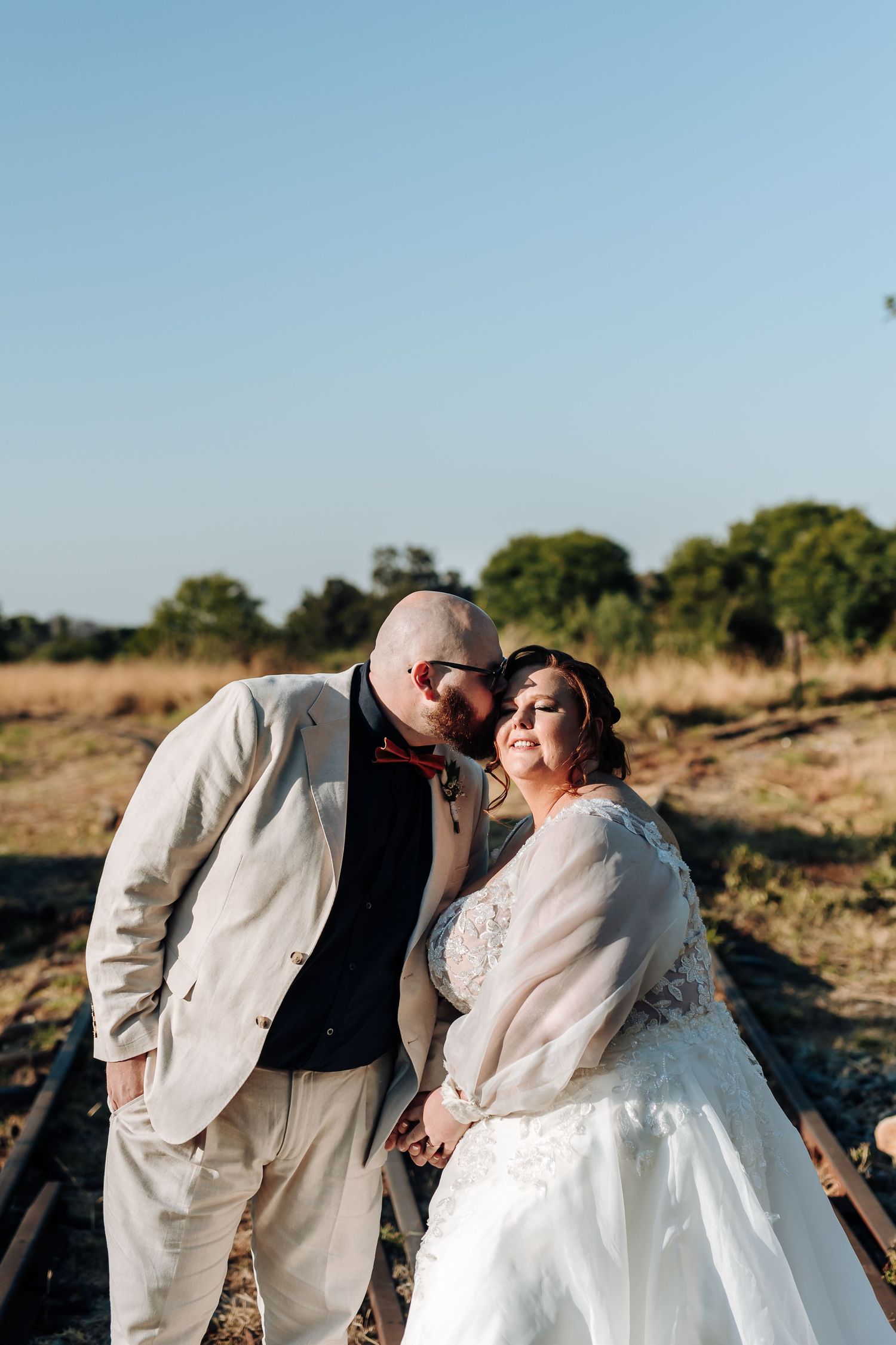 A couple shares a tender moment at sunset in a rustic outdoor setting.