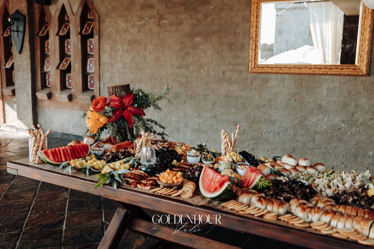 Elegant wedding grazing table with charcuterie, fruits, and floral arrangements at a rustic venue.