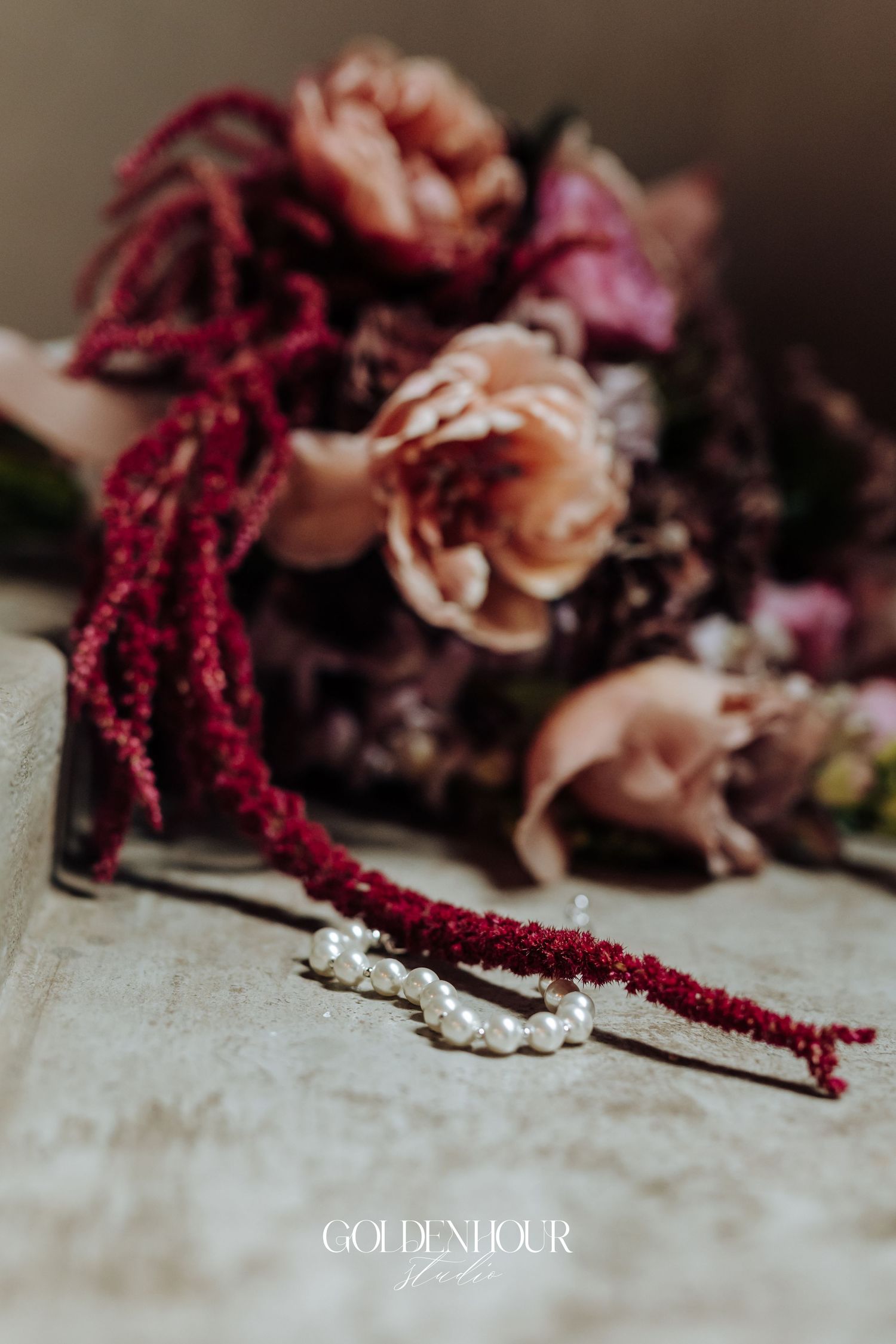 Pearl and burgundy amaranthus bridal earrings resting beside romantic mauve and crimson wedding bouquet.