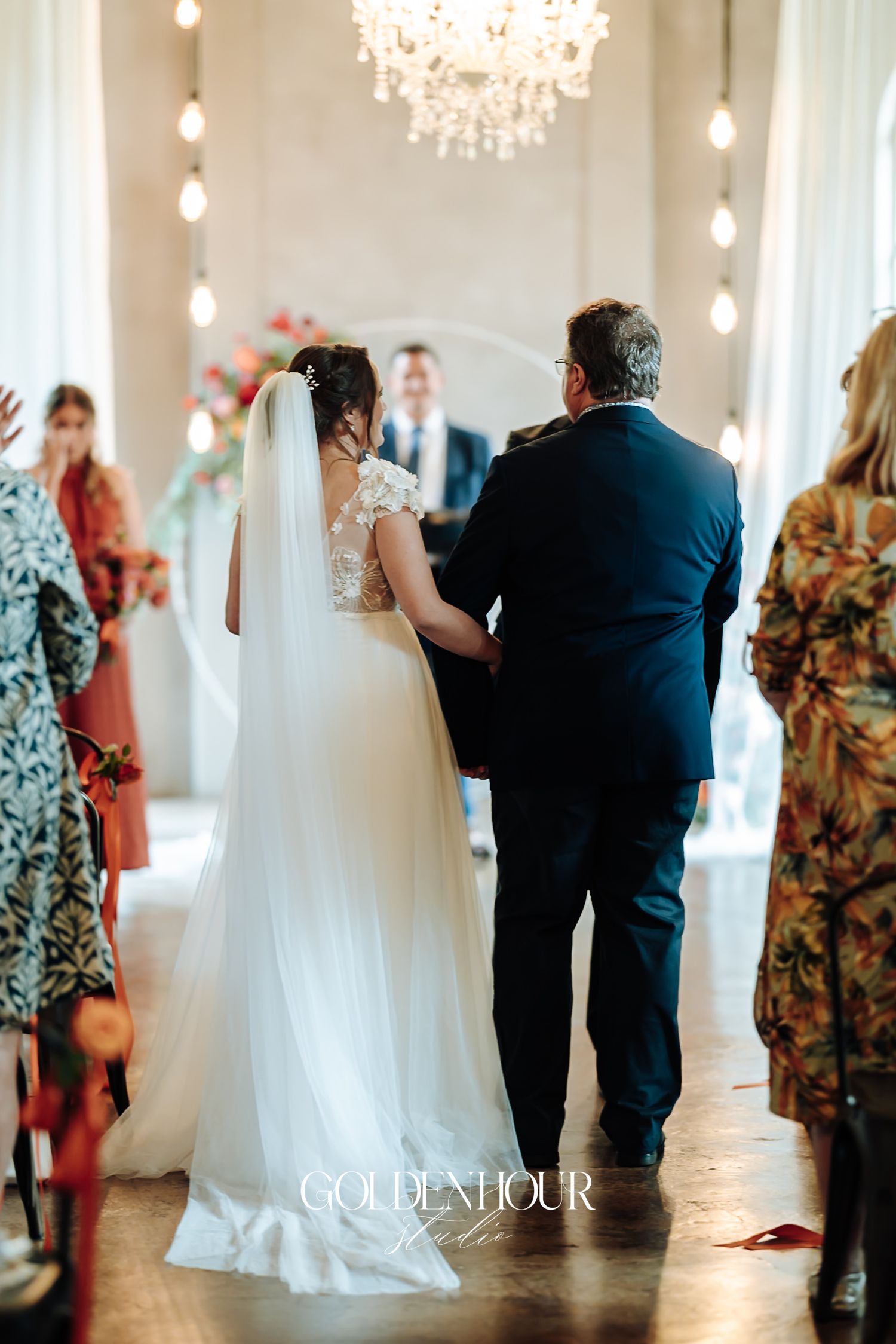 Bride in lace gown and veil walking down the aisle escorted by her father toward the altar.