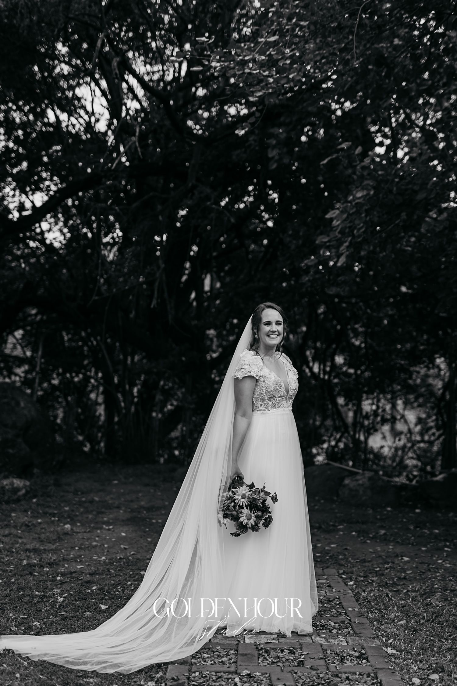 Black and white portrait of bride in lace gown with long cathedral veil holding bouquet.