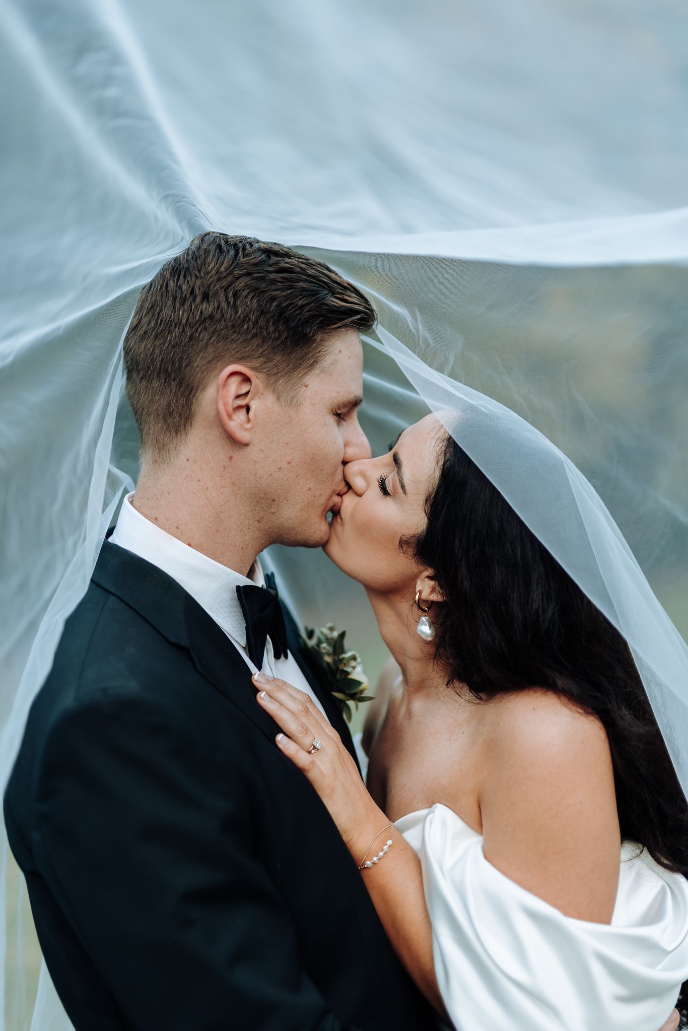 A romantic wedding kiss through a delicate white veil against a soft blue backdrop.
