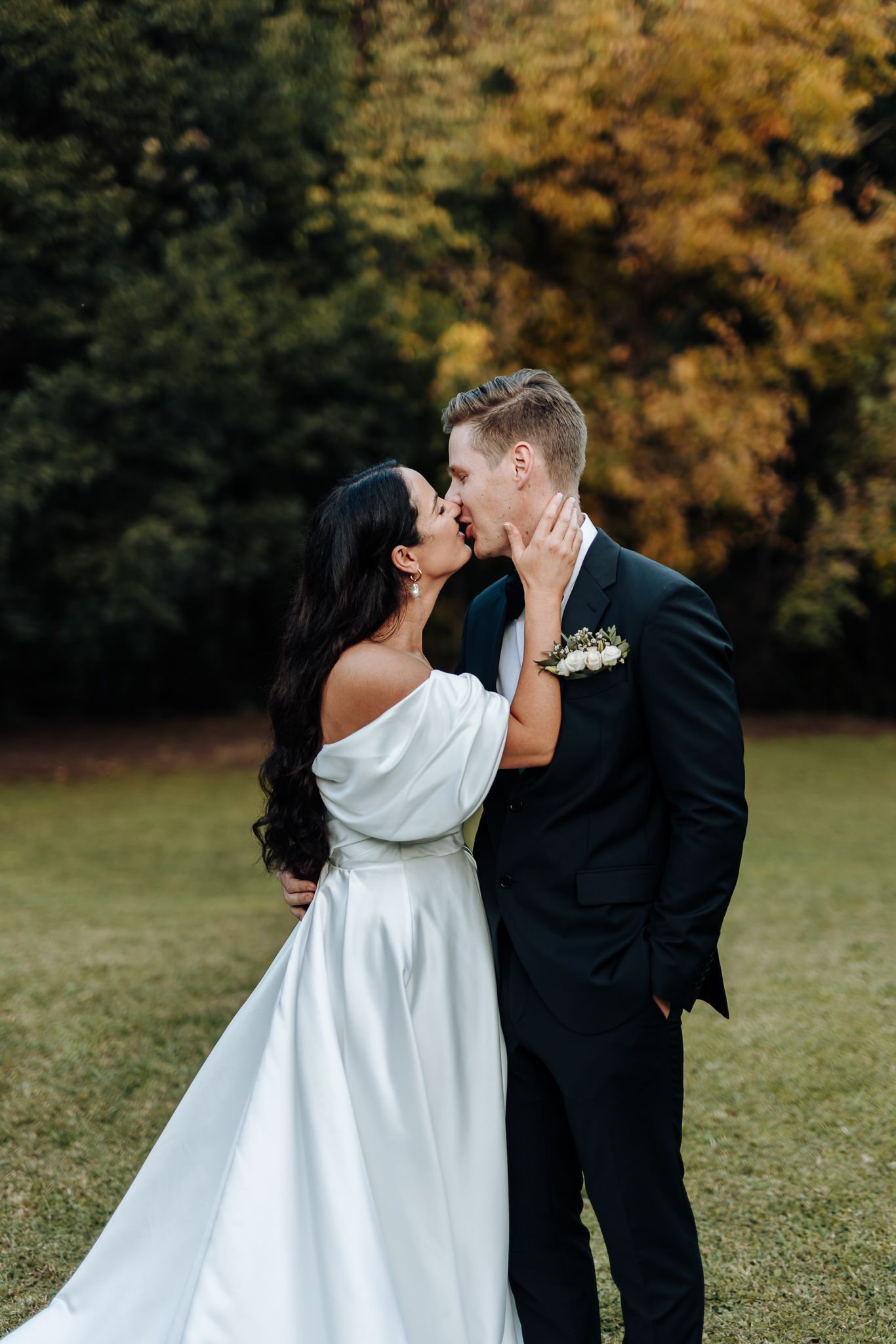 Intimate wedding portrait of couple embracing outdoors with fall foliage in background.