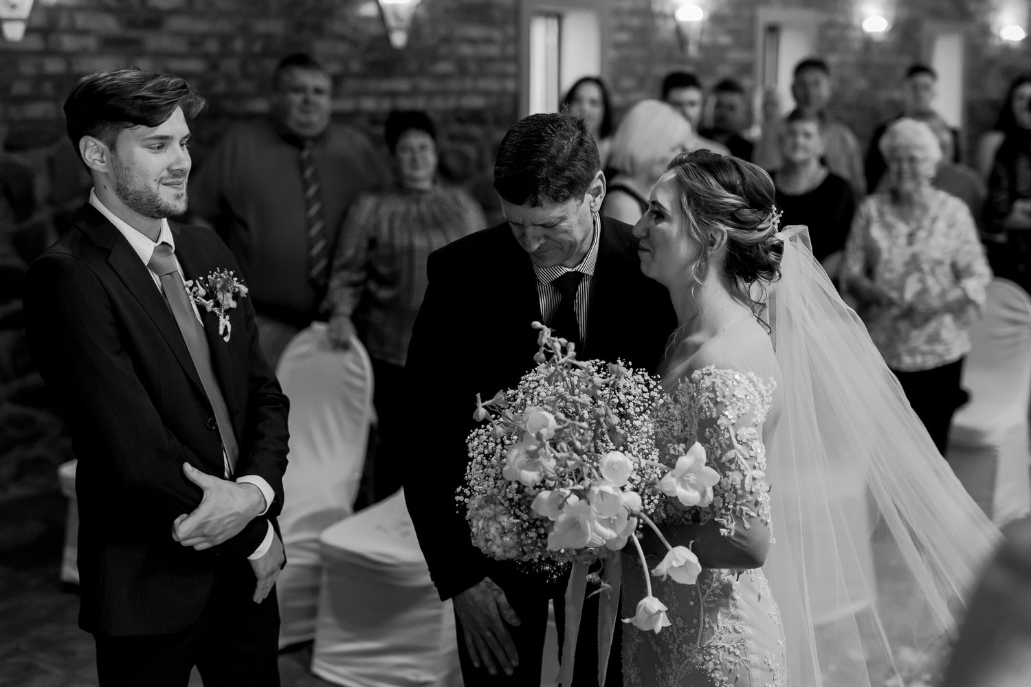 Black and white capture of intimate wedding ceremony moment inside rustic brick venue.