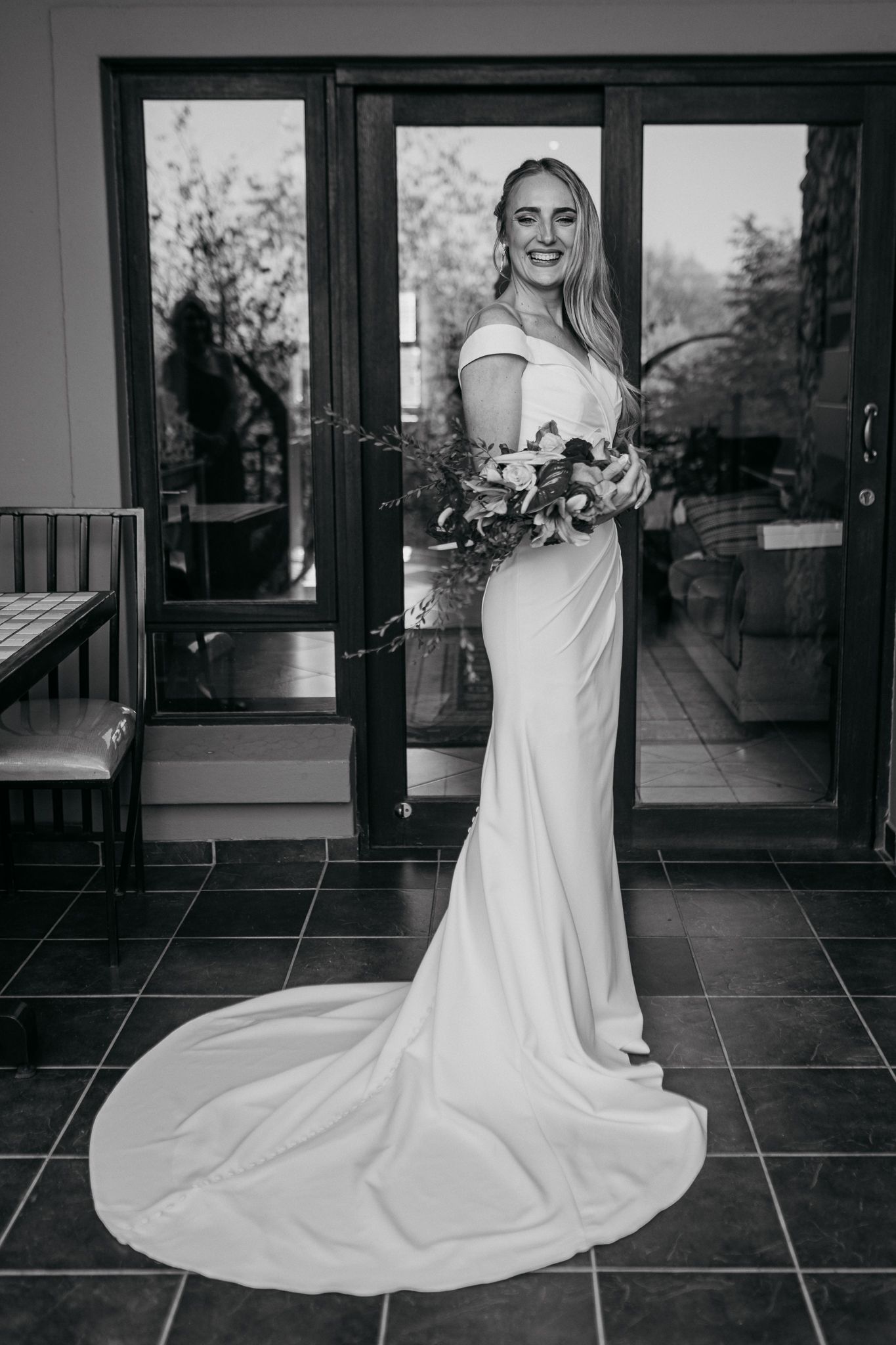 Black and white portrait of bride in flowing dress with train holding bouquet.