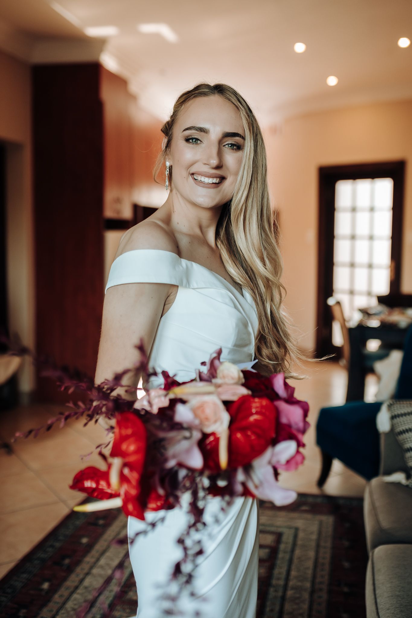 Radiant bridal portrait with red and pink bouquet in natural window light.