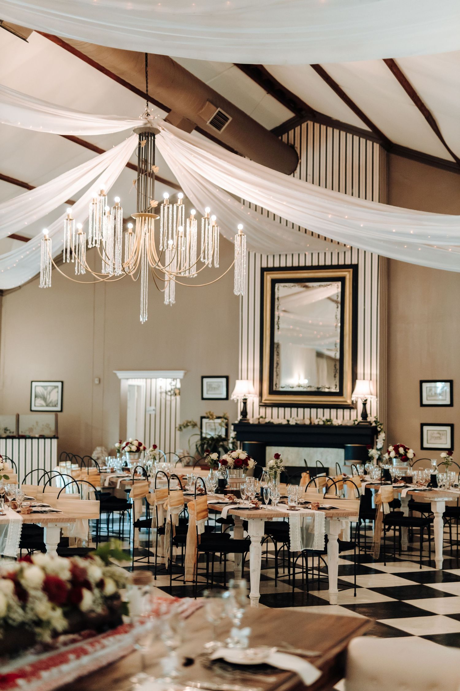 Elegant reception hall with draped white fabric, chandeliers, and checkered floor.