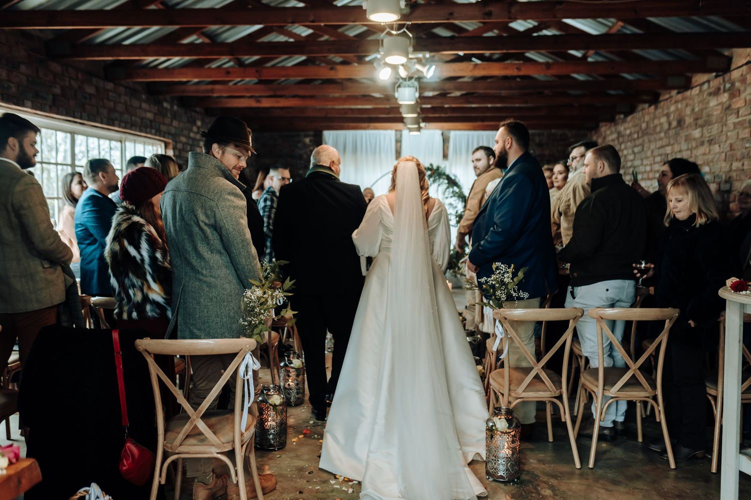 Wedding ceremony taking place in an industrial-style venue with exposed brick walls and wooden ceiling beams.