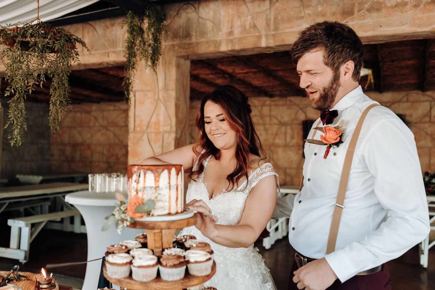 Newlyweds share a sweet moment while cutting their cupcake tower at a rustic wedding reception.