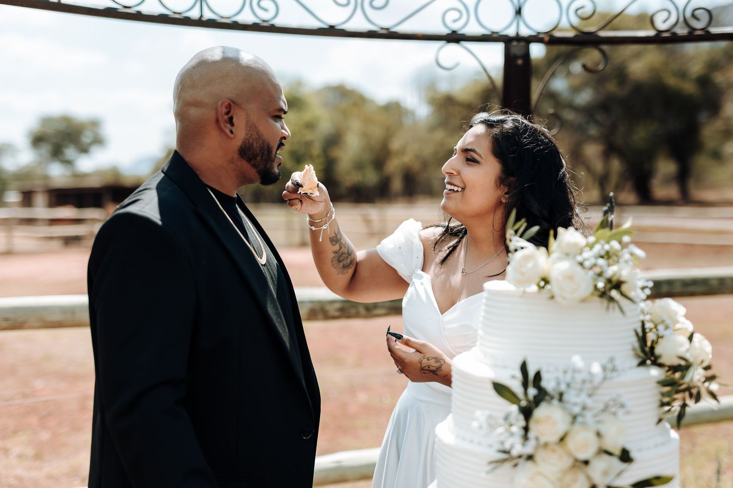 A joyful couple sharing cake during their wedding celebration outdoors.