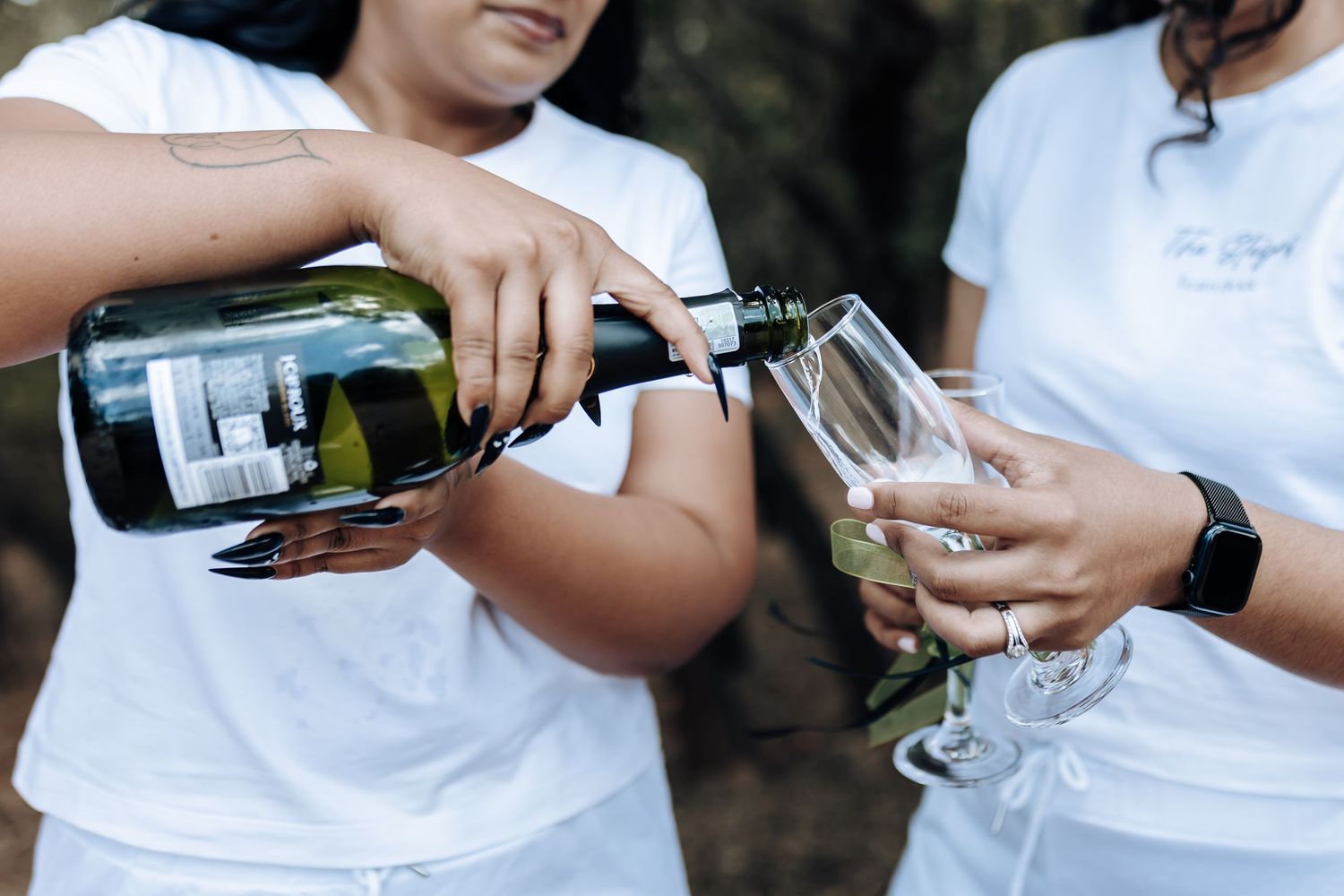 Pouring champagne into glasses while wearing matching white outfits outdoors.