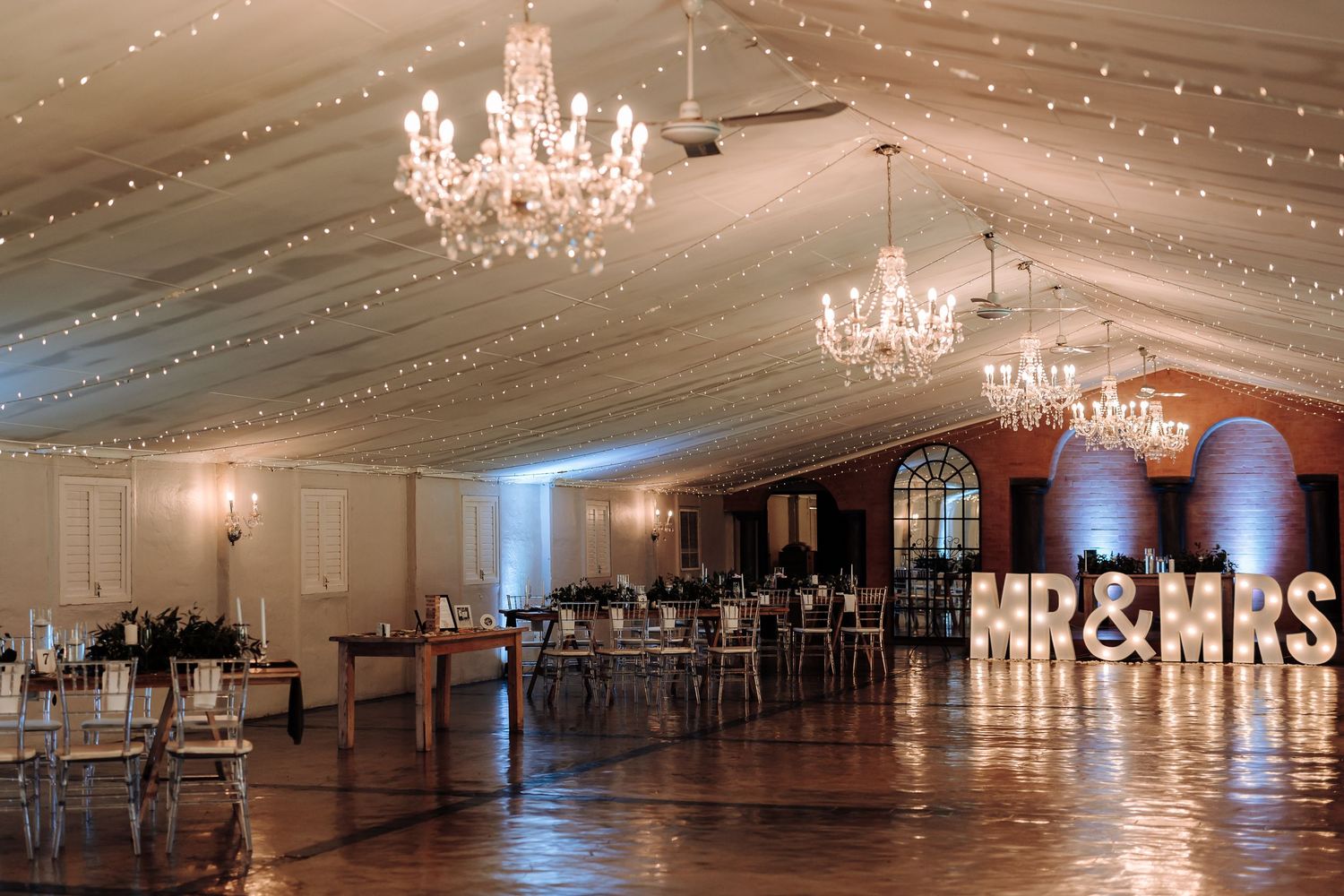 Elegant ballroom with crystal chandeliers and string lights creating a romantic wedding reception atmosphere.