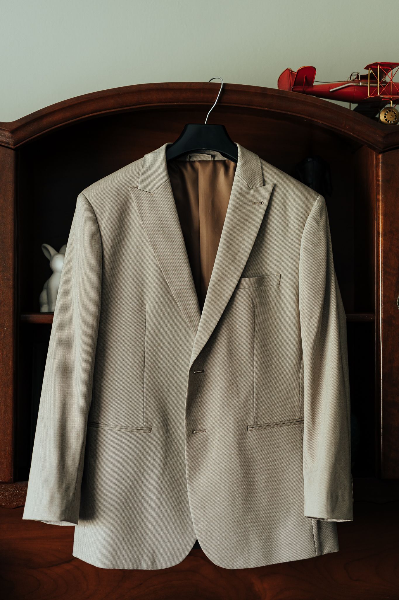 Light beige suit jacket hanging on wooden hanger in an elegant wardrobe.