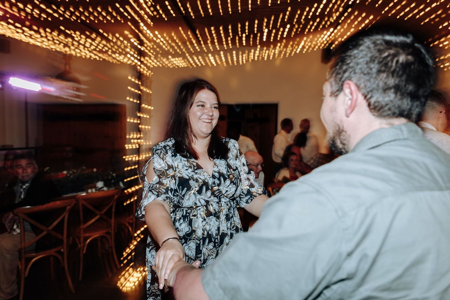 Couples dance together under a warm glowing ceiling of string lights at an elegant evening celebration.