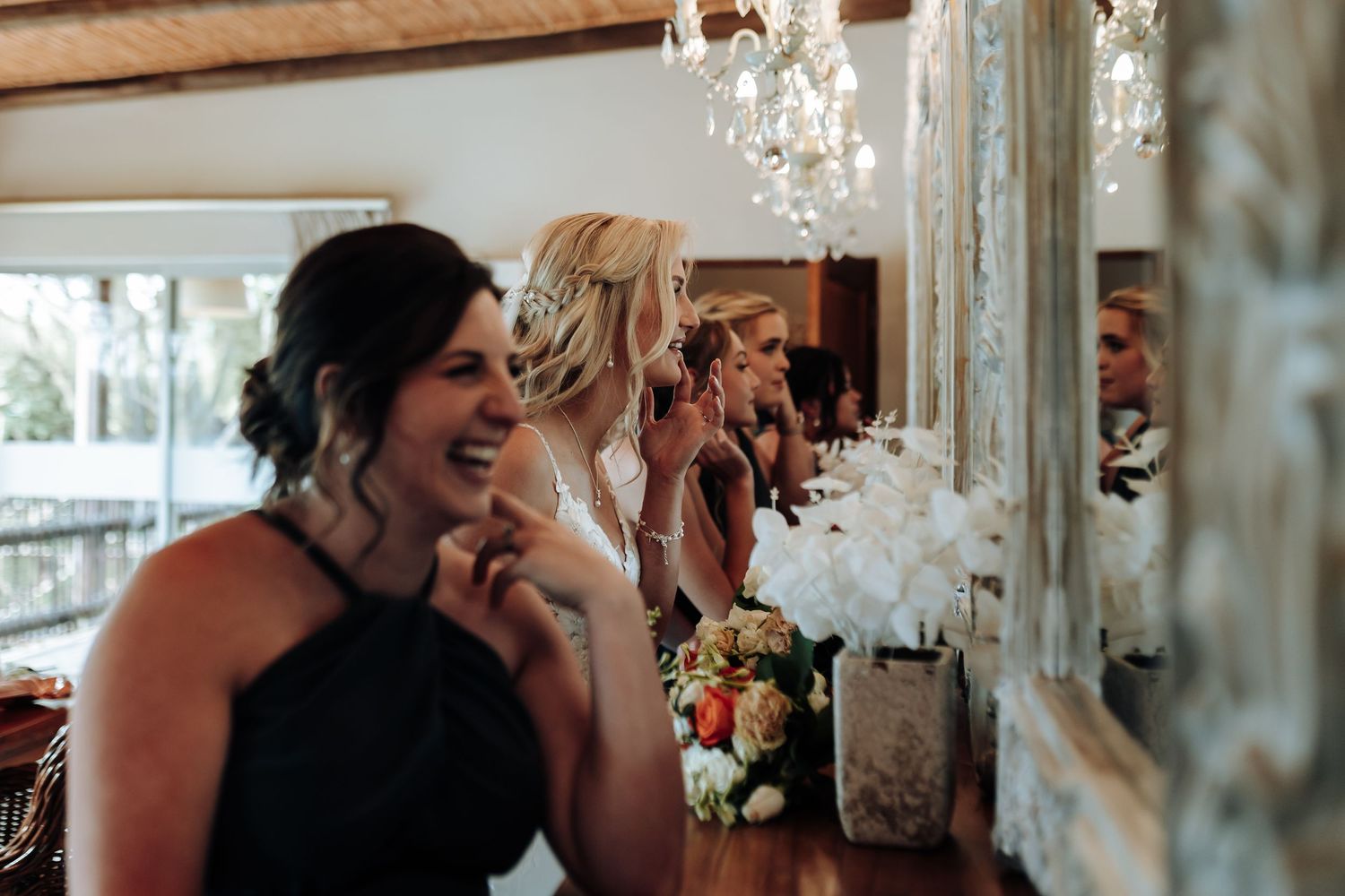 Guests celebrate at an elegant wedding reception under crystal chandeliers with floral arrangements and warm lighting.