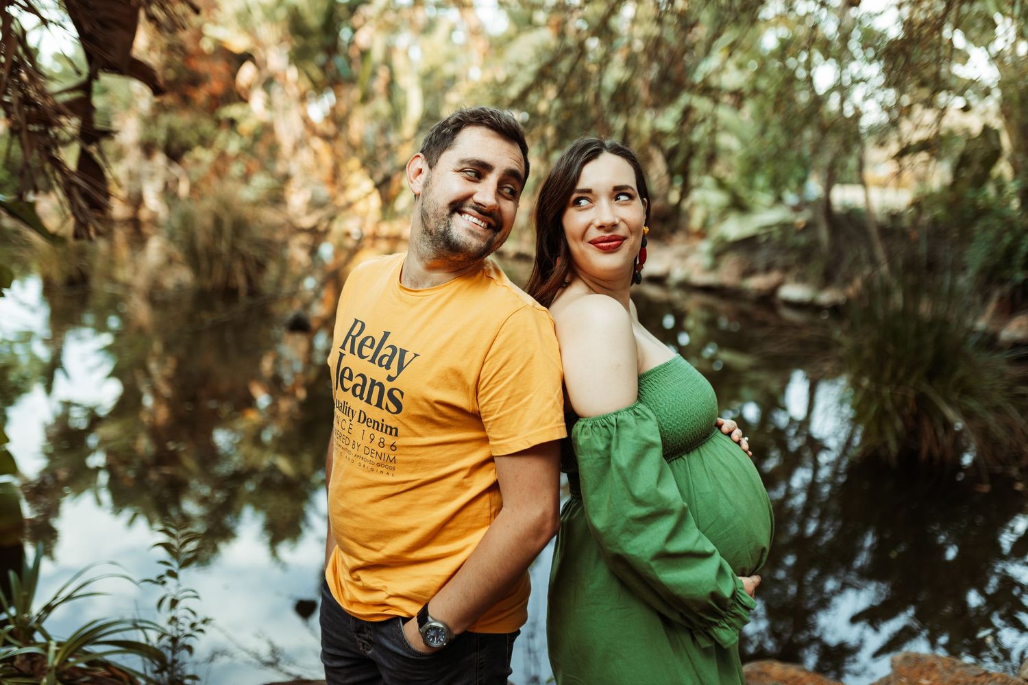Couple in yellow and green outfits share romantic moments during outdoor photo session in wooded setting.